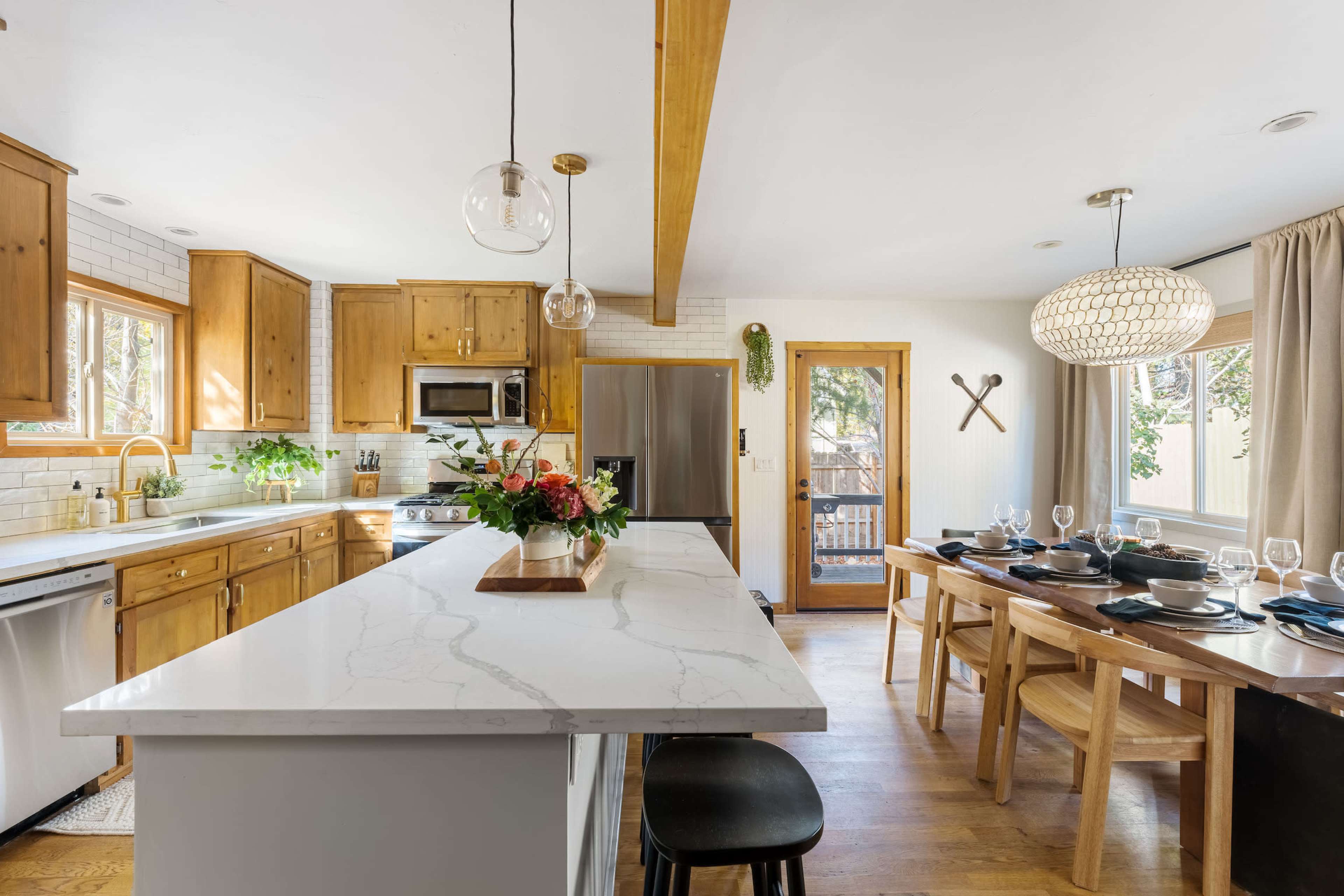 A modern kitchen features wooden cabinetry, a marble countertop island, and a dining area with a wooden table set for a meal.