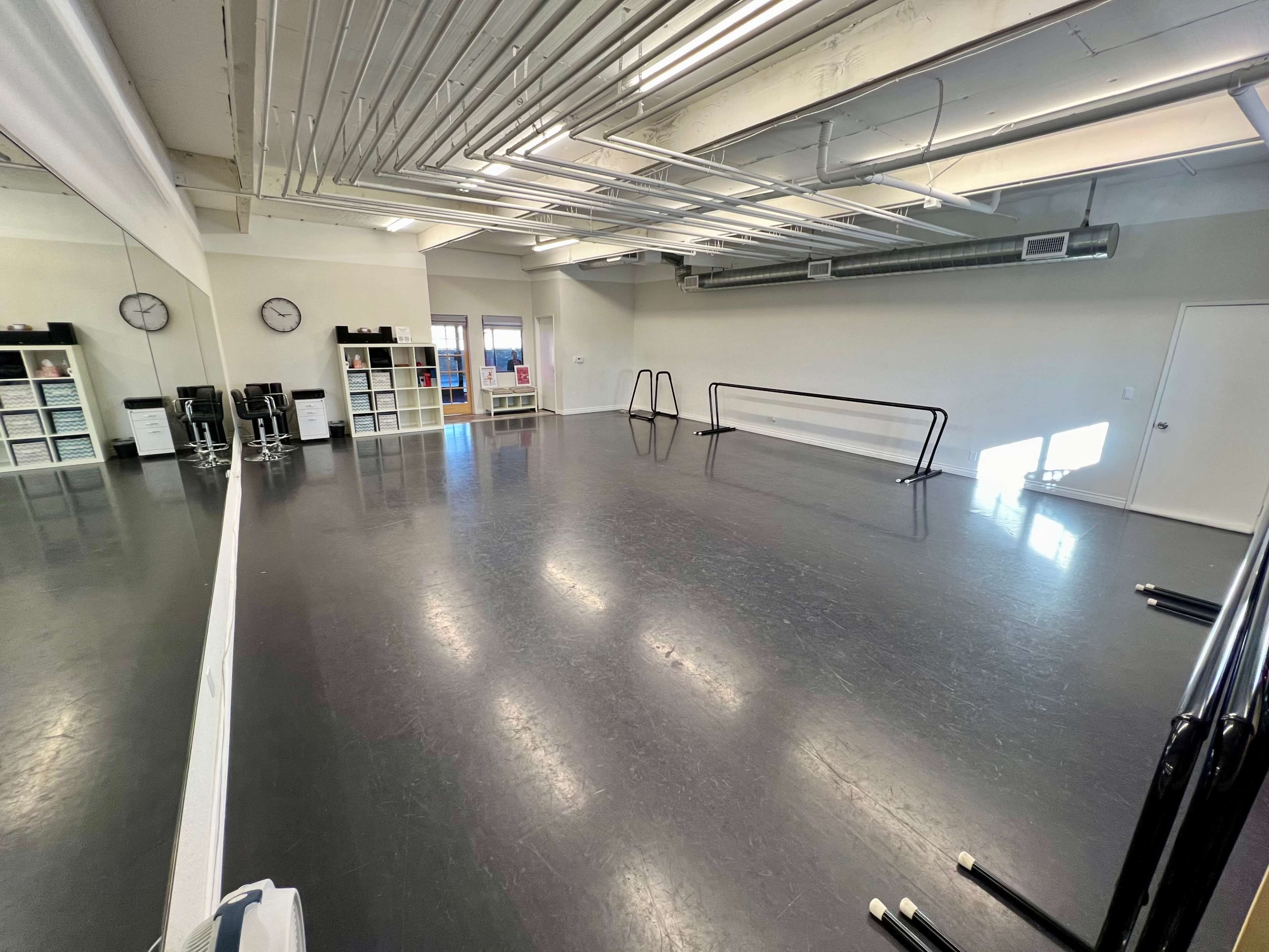 A spacious dance studio with a polished floor, mirrors on one wall, and two ballet barres along the opposite side.