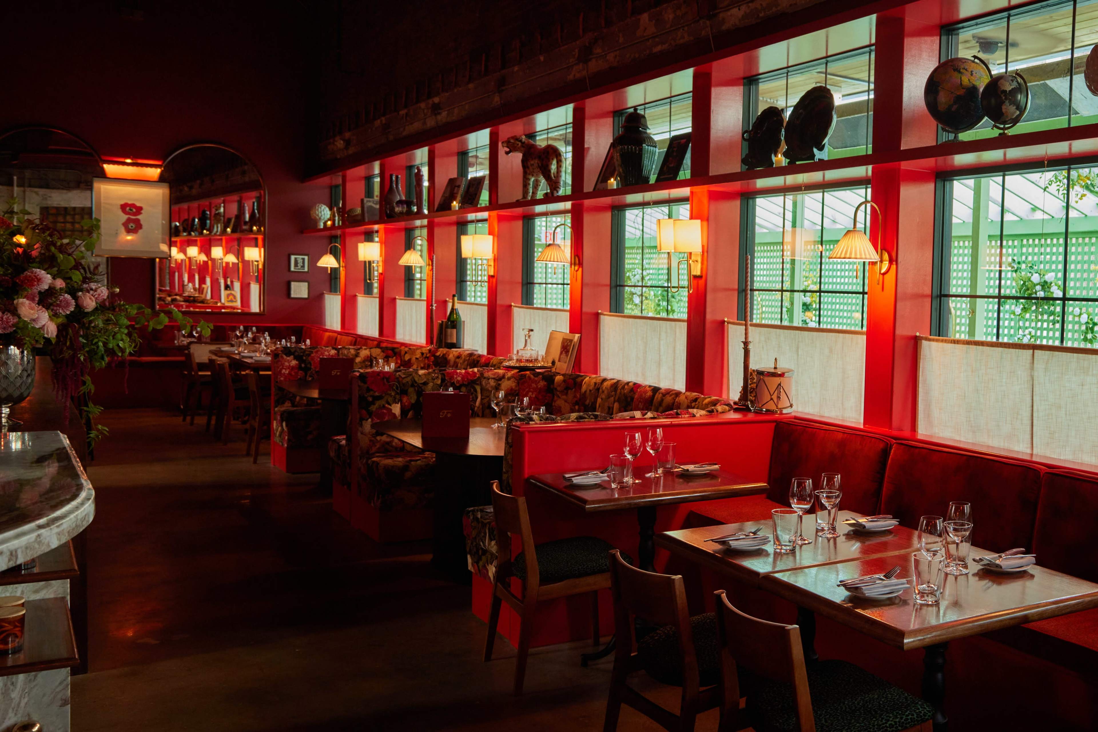 The image shows a brightly lit restaurant featuring red walls, wooden tables, and decorative elements such as vintage globes and floral arrangements.