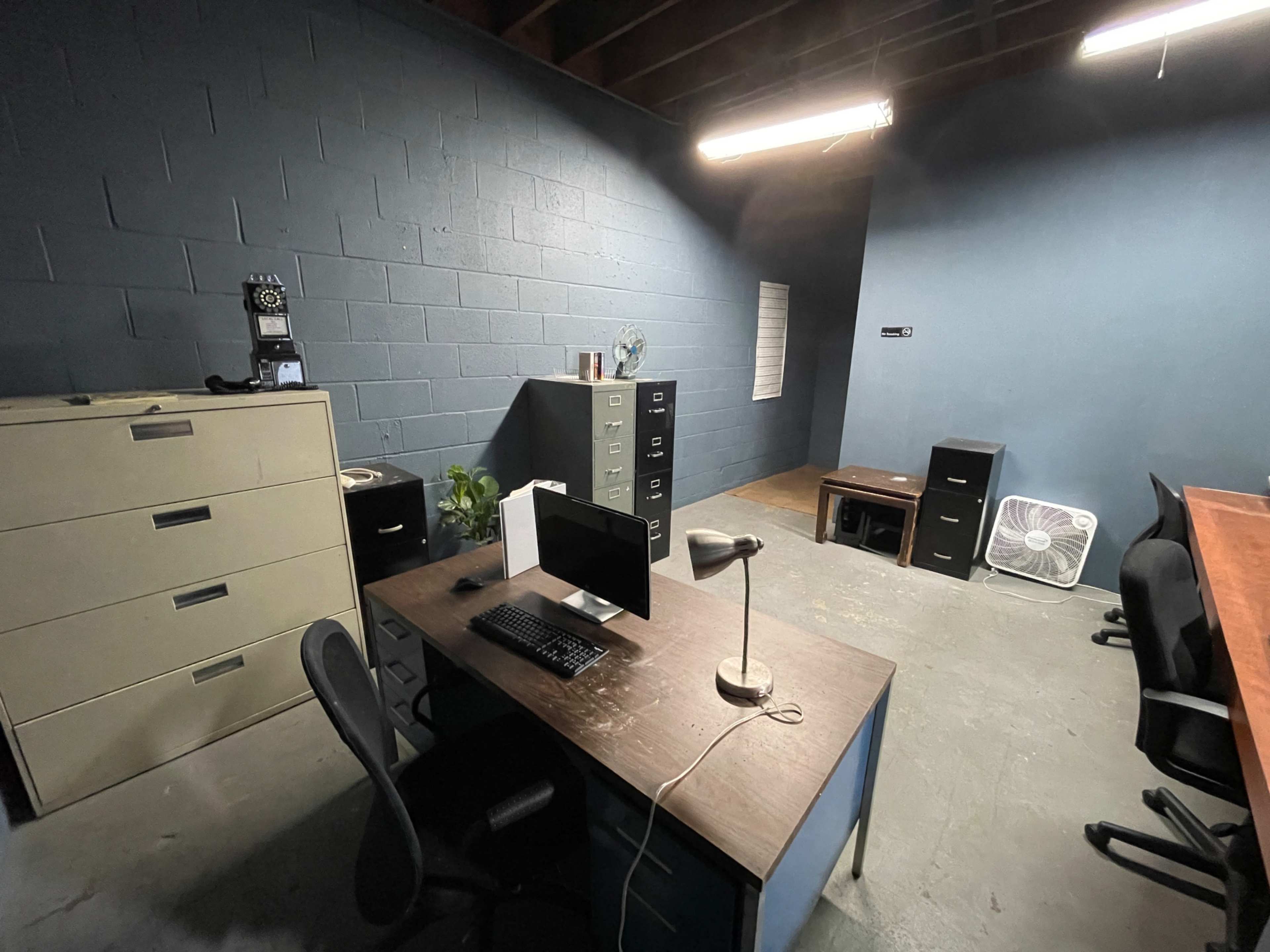 The image shows an office space with a desk, computer, filing cabinets, and chairs arranged in a minimalistic layout.