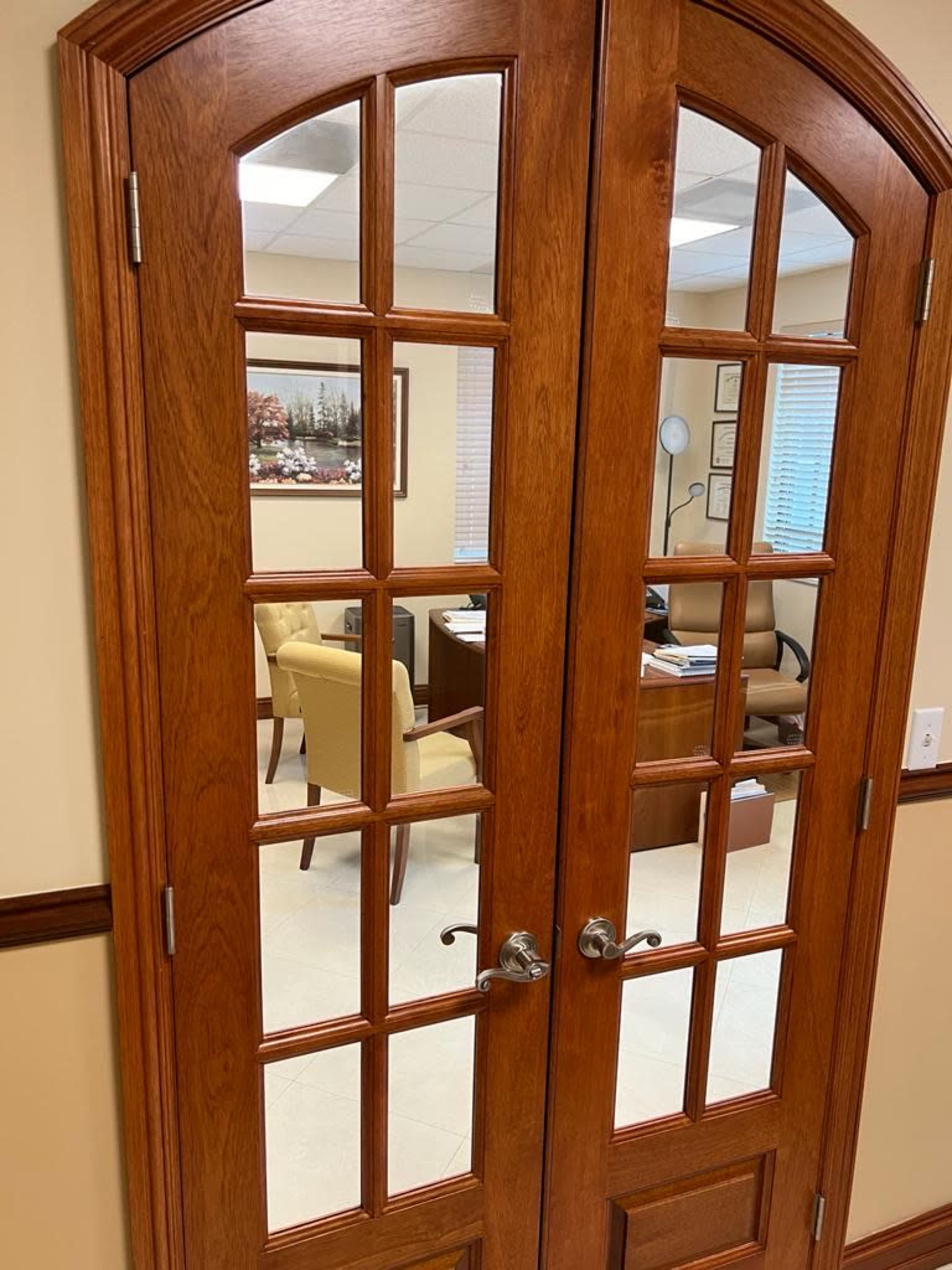 A wooden double door with glass panels, leading into an office space furnished with chairs and a desk.