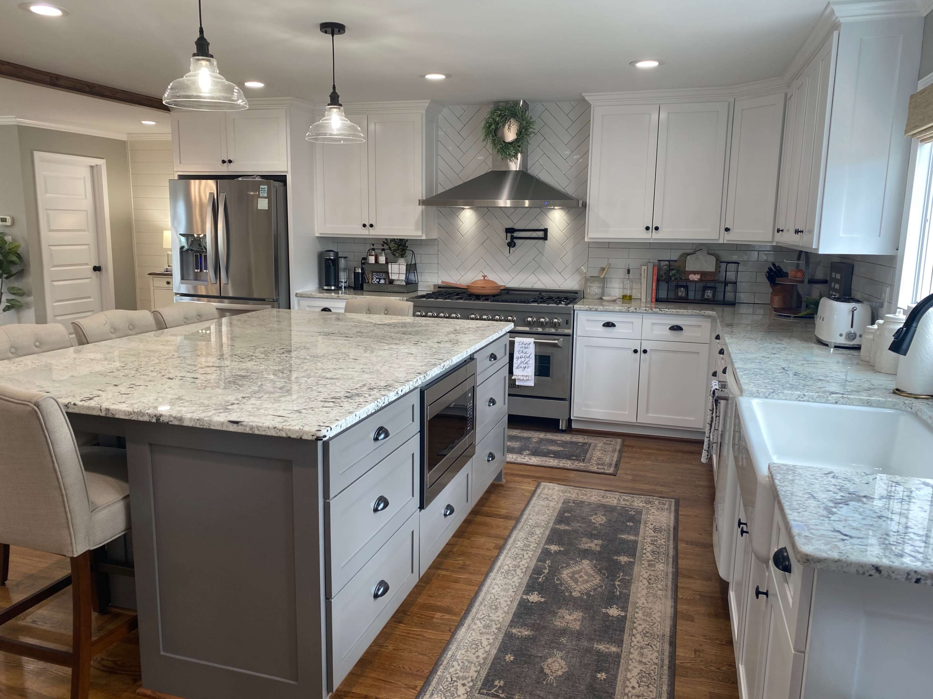 The kitchen features a large island with a gray base, white cabinetry, granite countertops, a stainless steel stove, and a farmhouse sink.