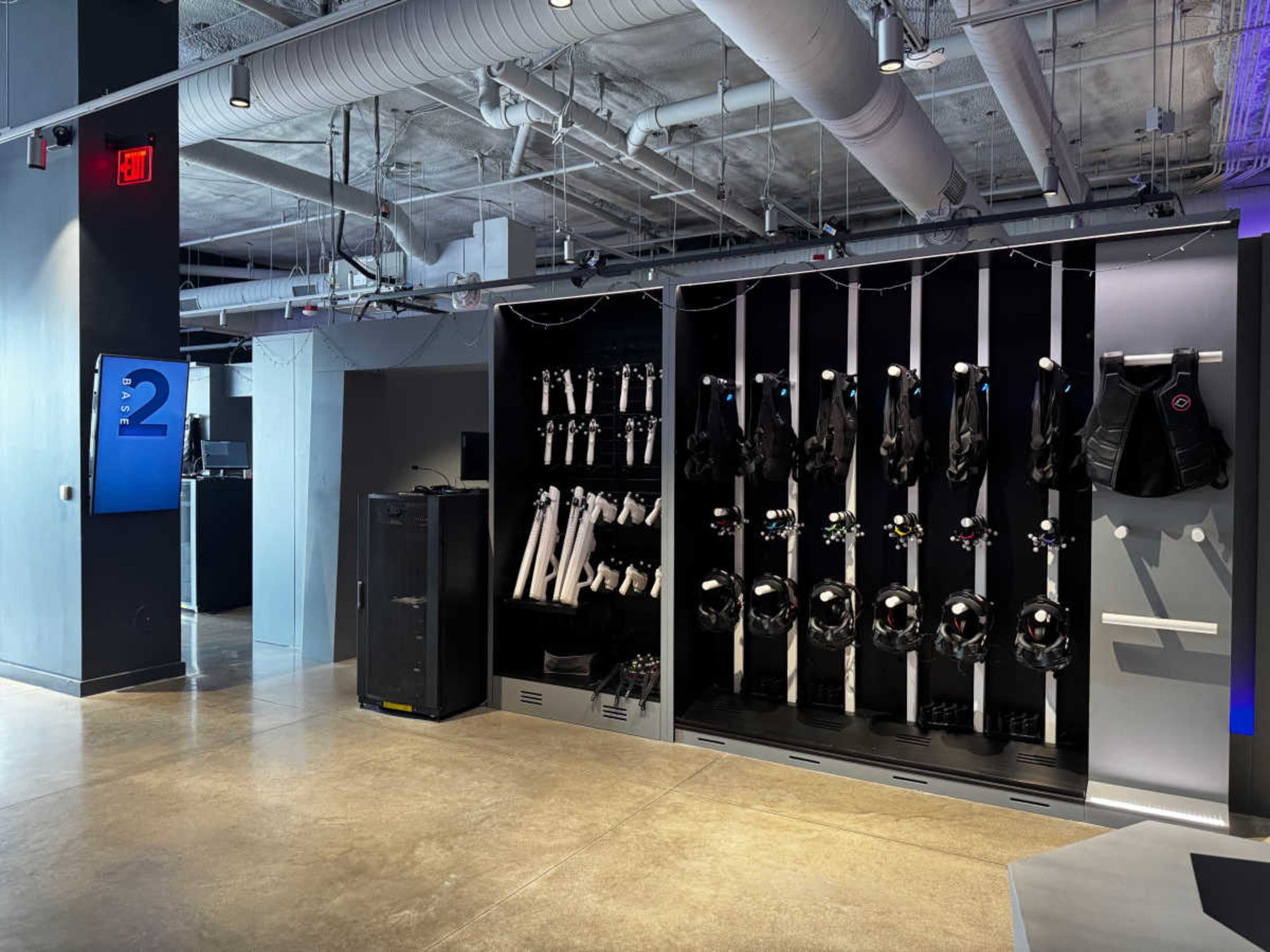The image shows a modern industrial space with a polished concrete floor and a wall featuring organized equipment, including harnesses and helmets, alongside a black cabinet.