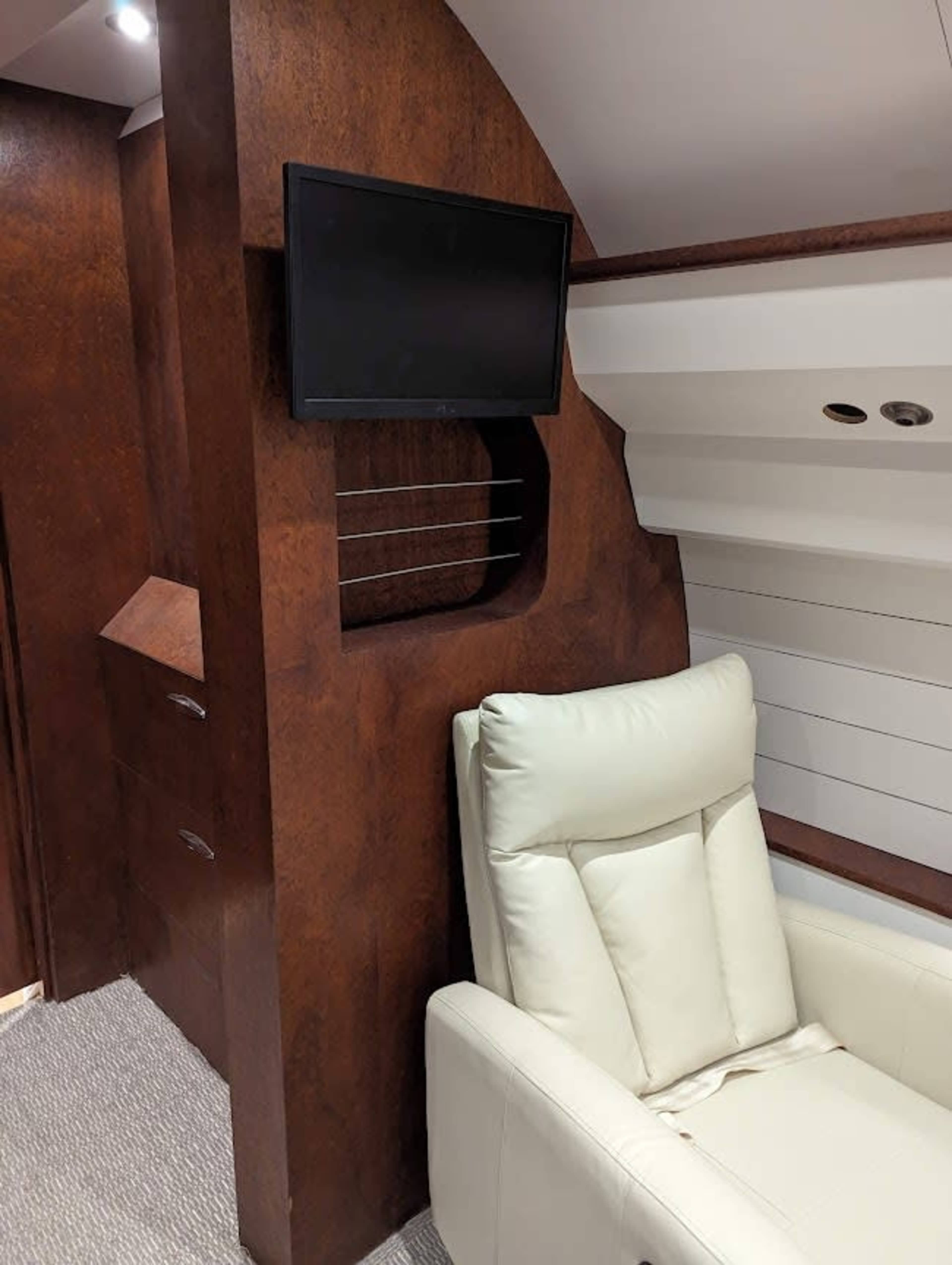 A luxurious aircraft interior with a wooden panel, a flat-screen TV mounted on the wall, and a white leather recliner.