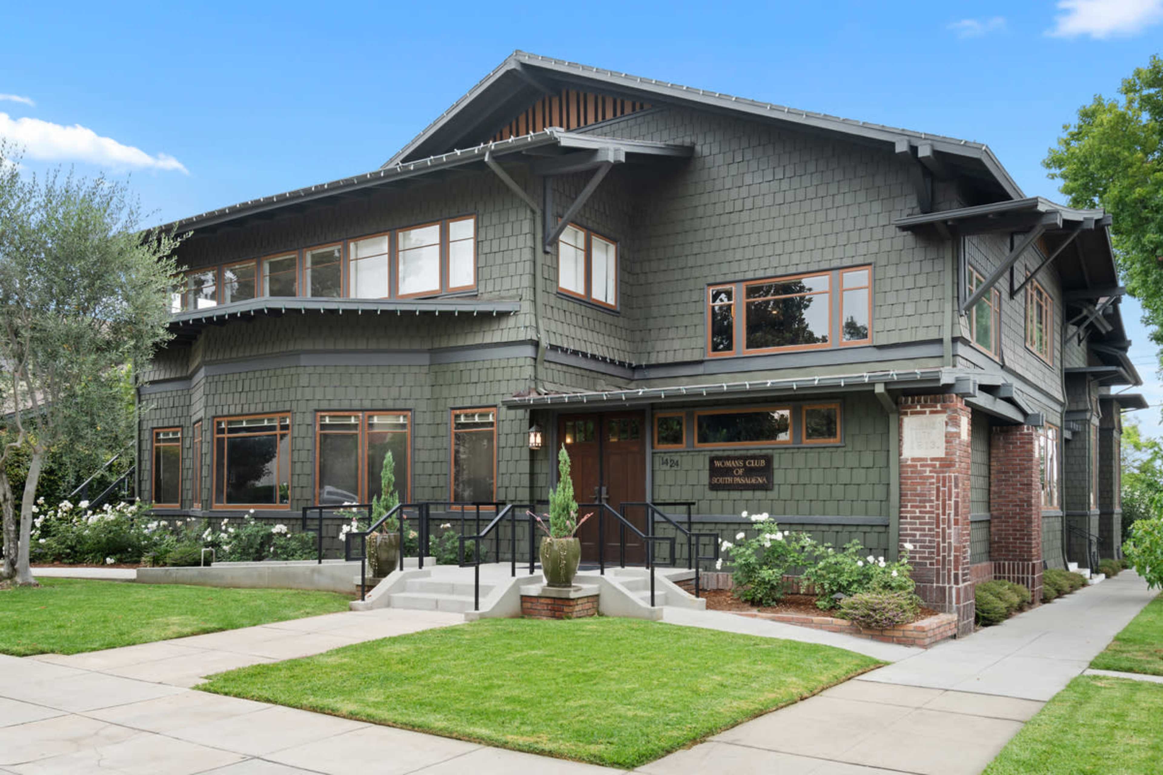 The image showcases a large, two-story Craftsman-style house with dark green shingles, multiple windows, and landscaped front steps.