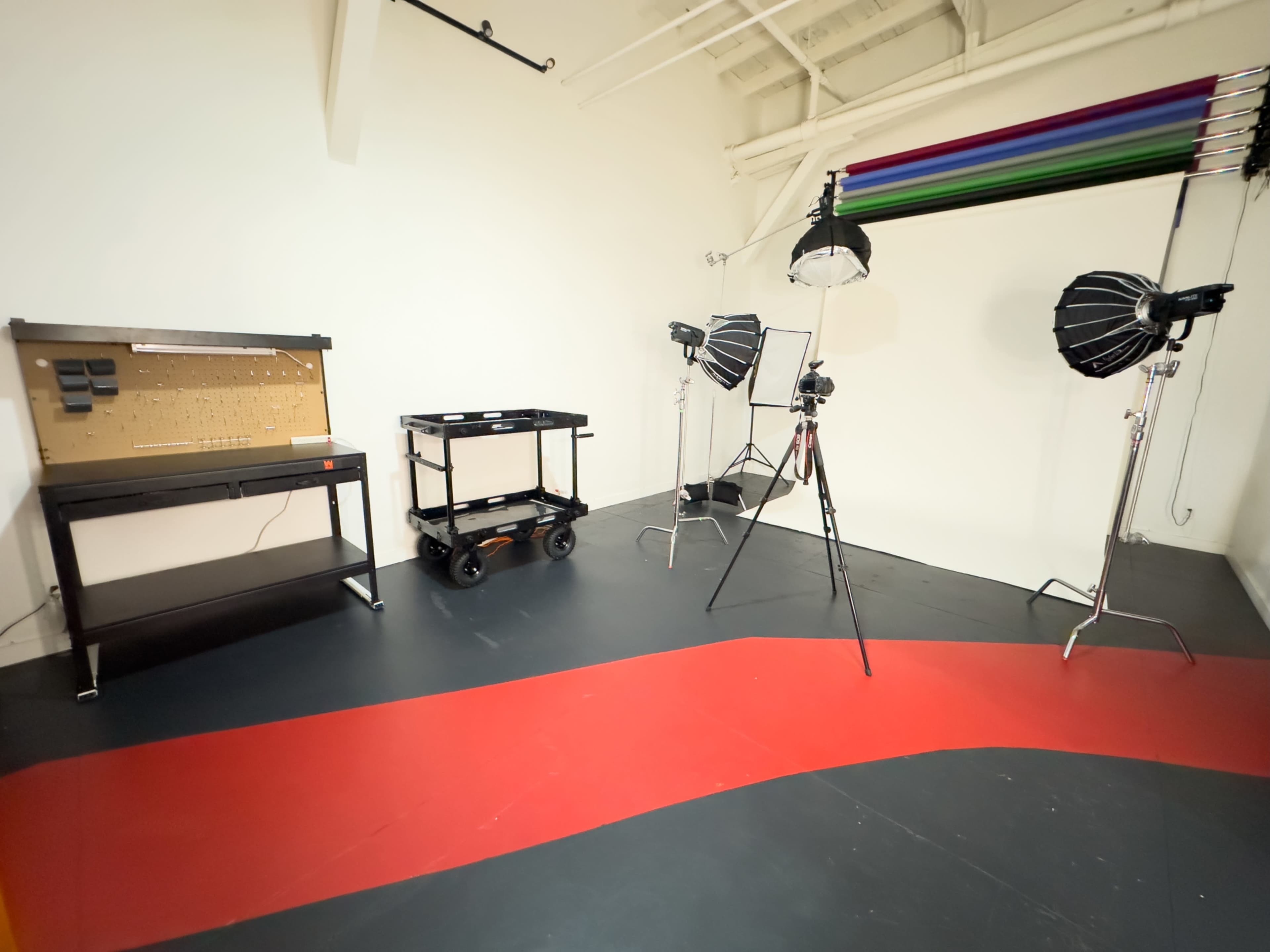 The image shows a photography studio equipped with lighting equipment, a cart, and a backdrop support system.