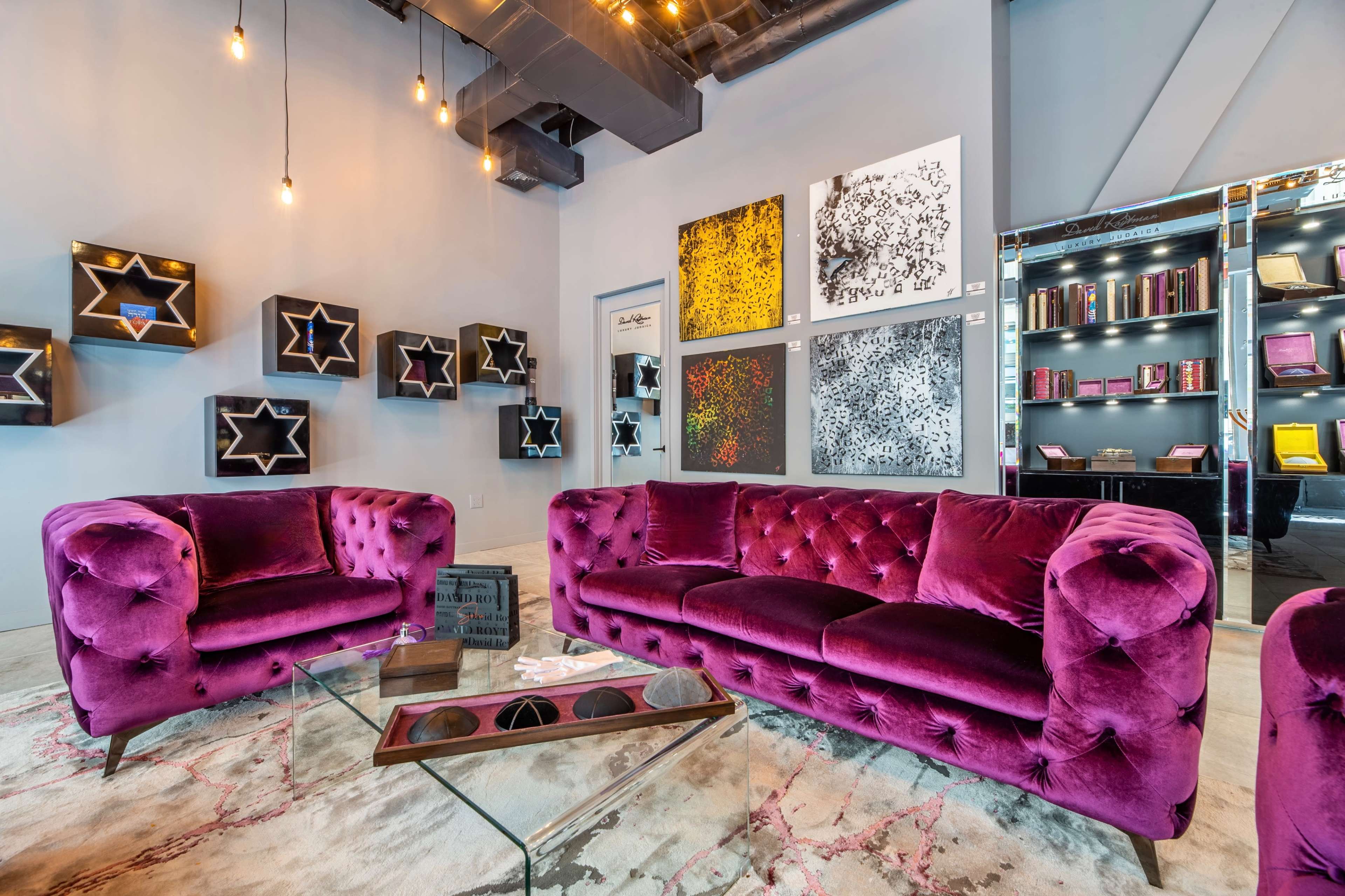 A modern lounge area features a plush violet couch, a glass coffee table, and artwork displayed on the walls.