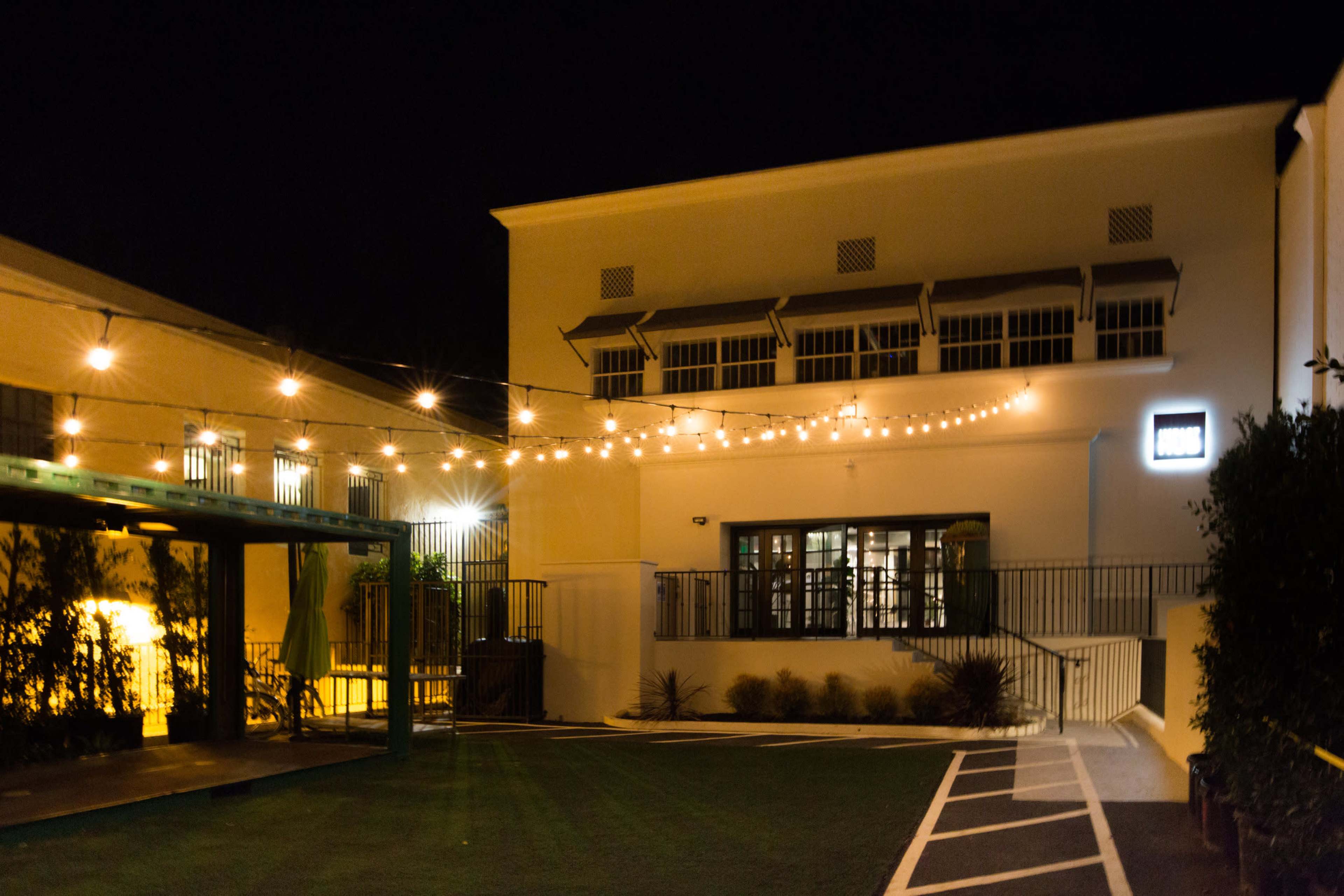 The image shows a well-lit outdoor space at night, with string lights illuminating a building and a green lawn area.