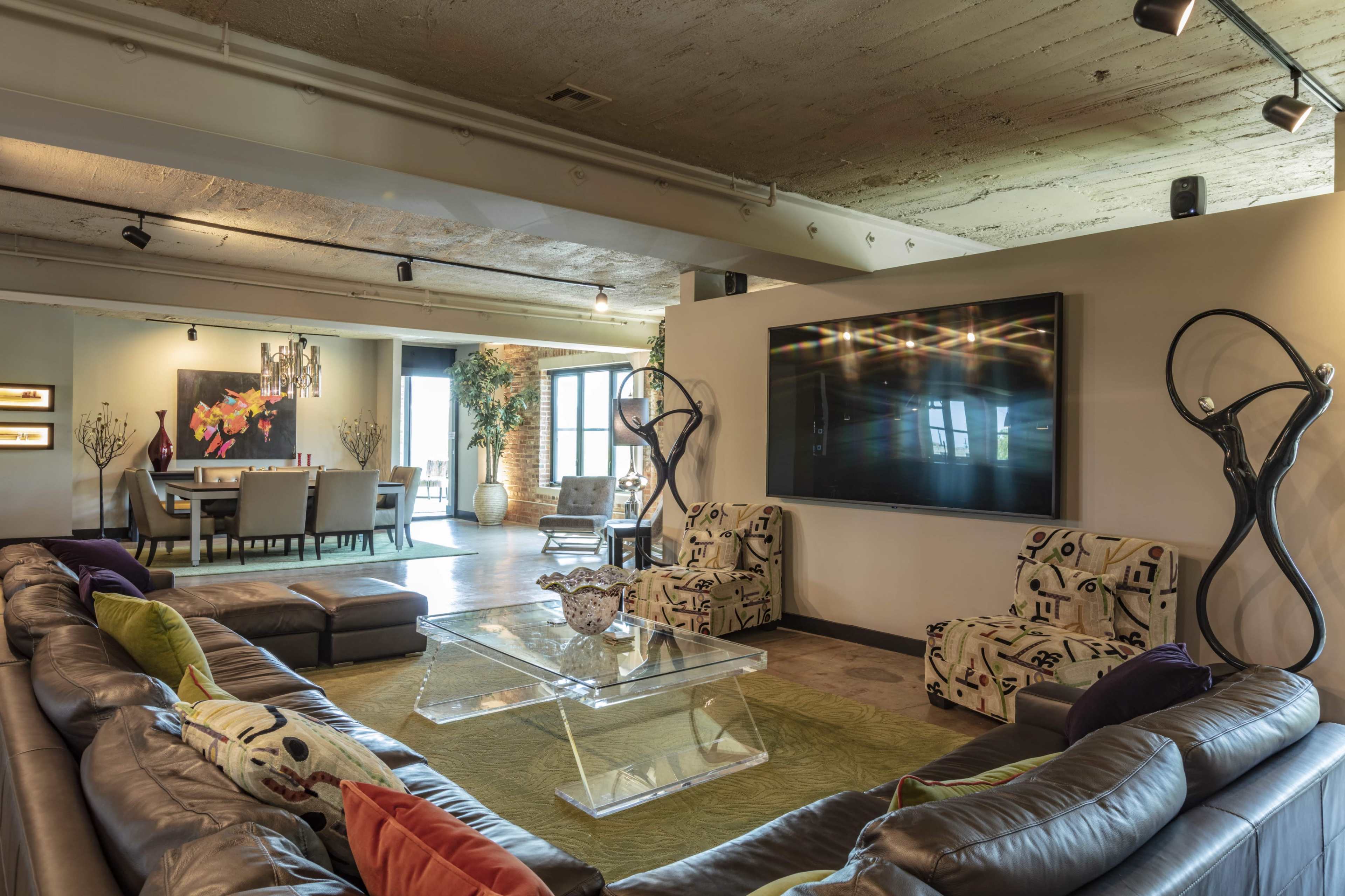 A spacious modern living room with a large sectional sofa, a glass coffee table, and a mounted television, leading into a dining area.