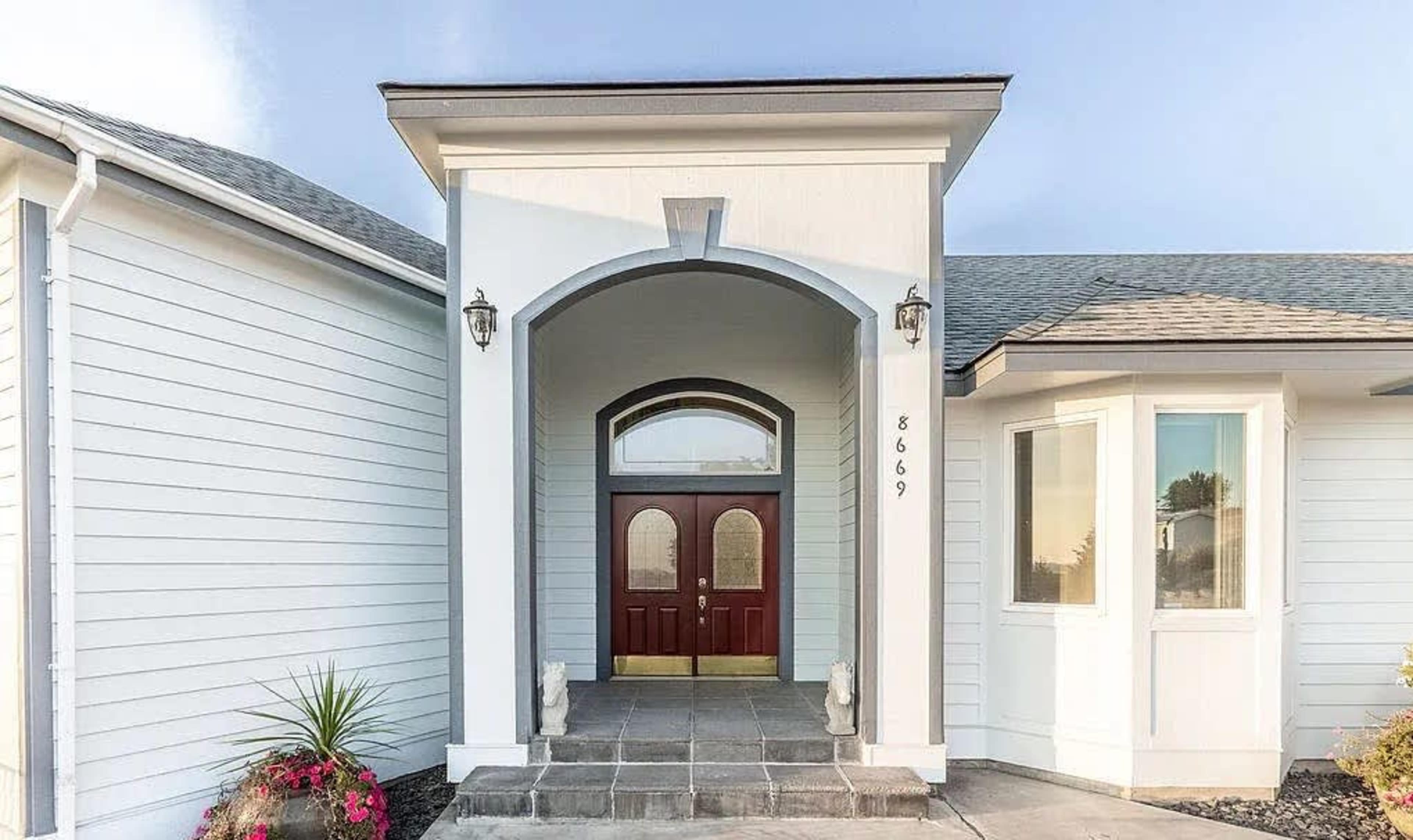 The entrance of a house featuring a large, arched doorway with double wooden doors flanked by two lanterns.