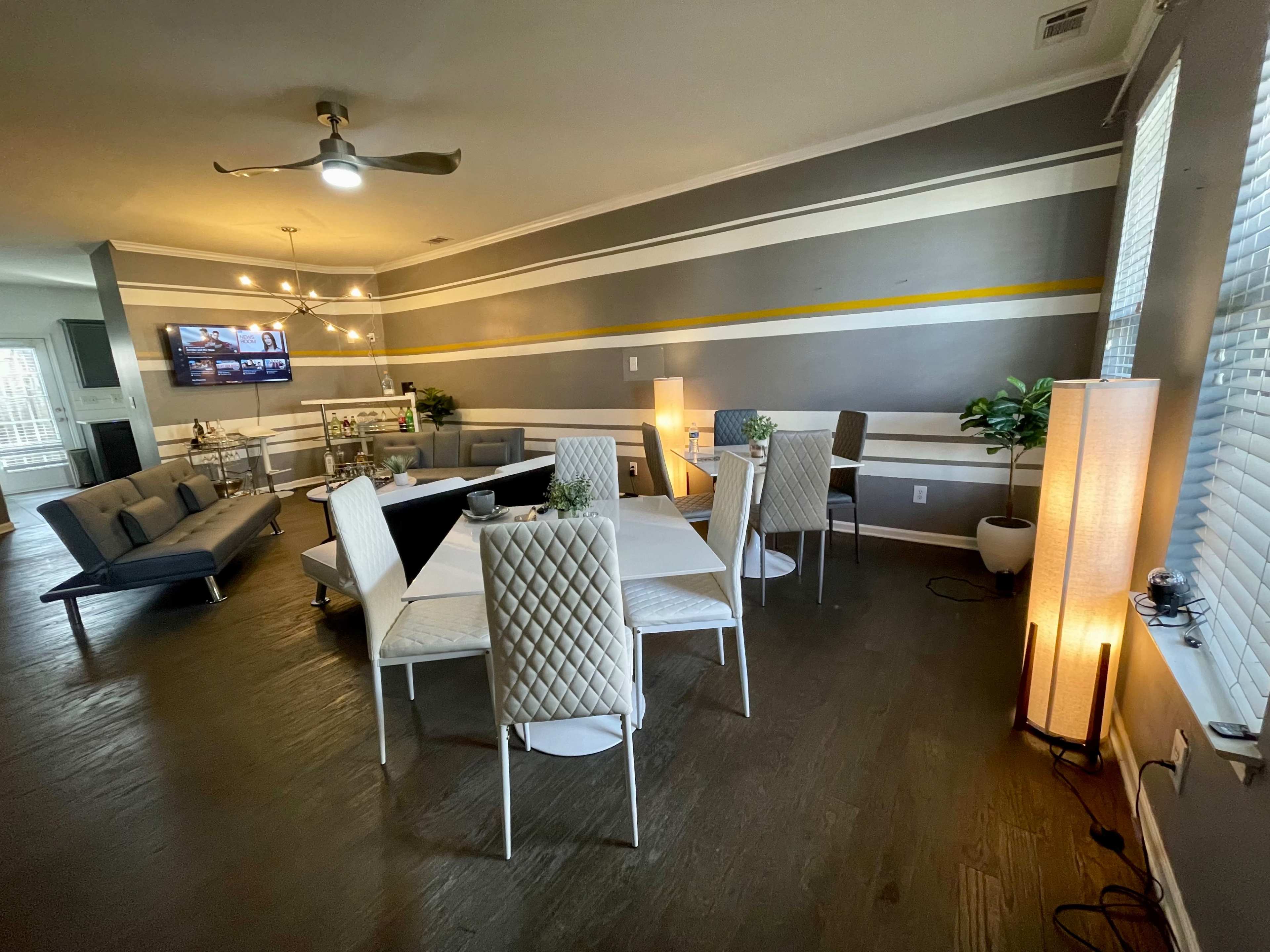 A modern living space with a dining table, white chairs, a sectional sofa, and ambient lighting.