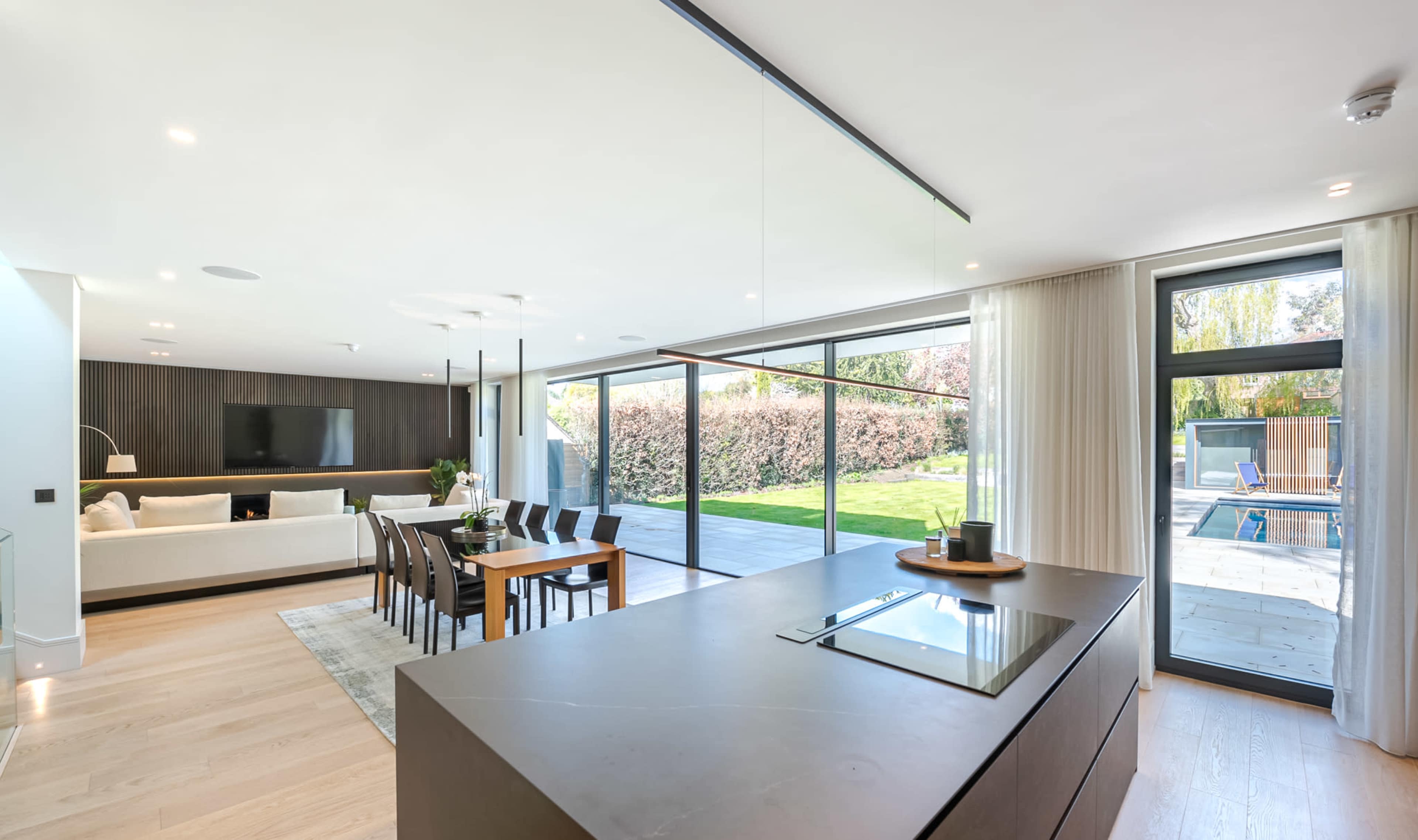 A modern, open-plan kitchen and dining area that connects to a spacious outdoor patio through large glass sliding doors.
