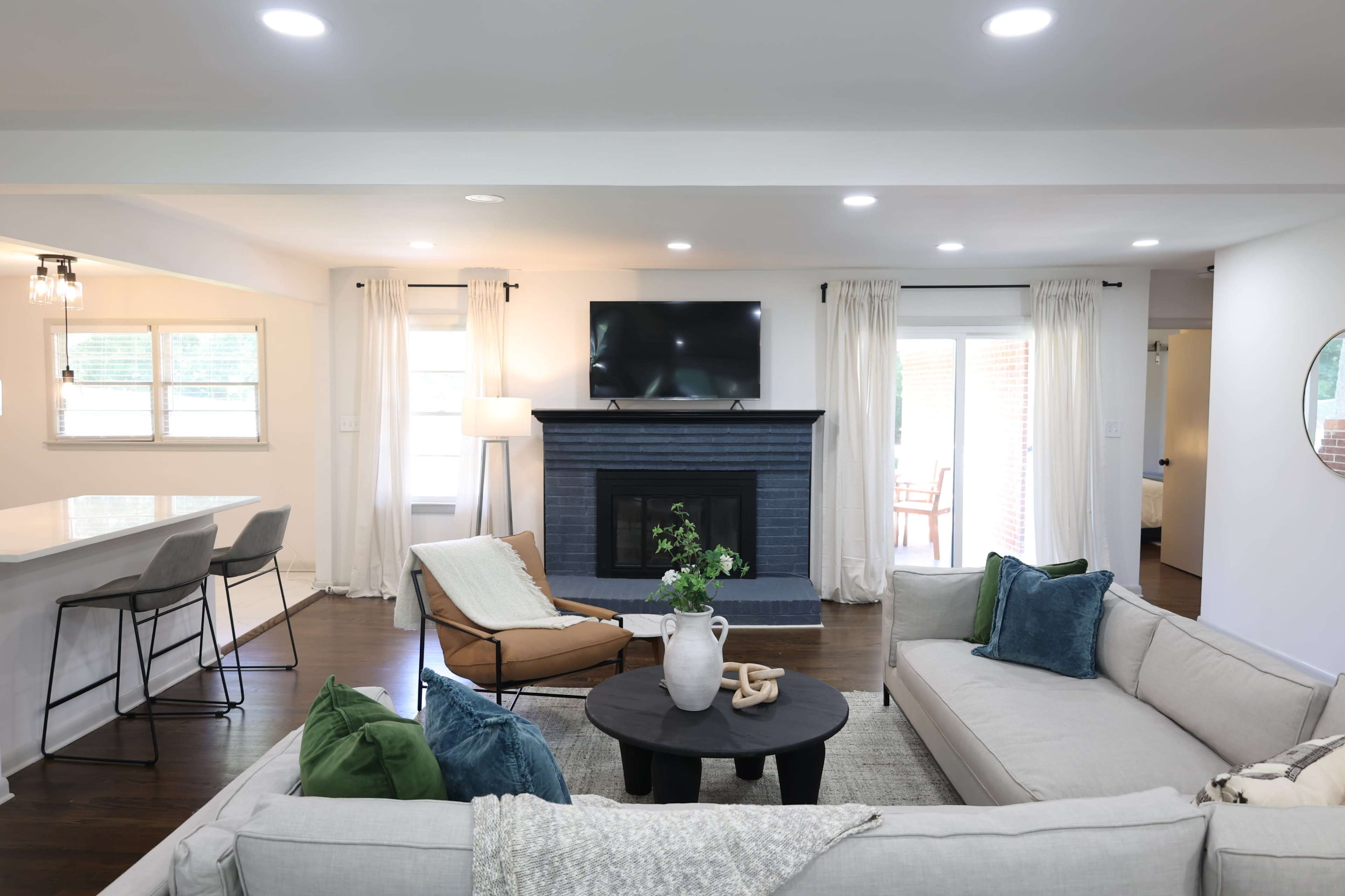 A modern living room with a gray fireplace, a TV mounted on the wall, a large sectional sofa, and a dining area visible in the background.