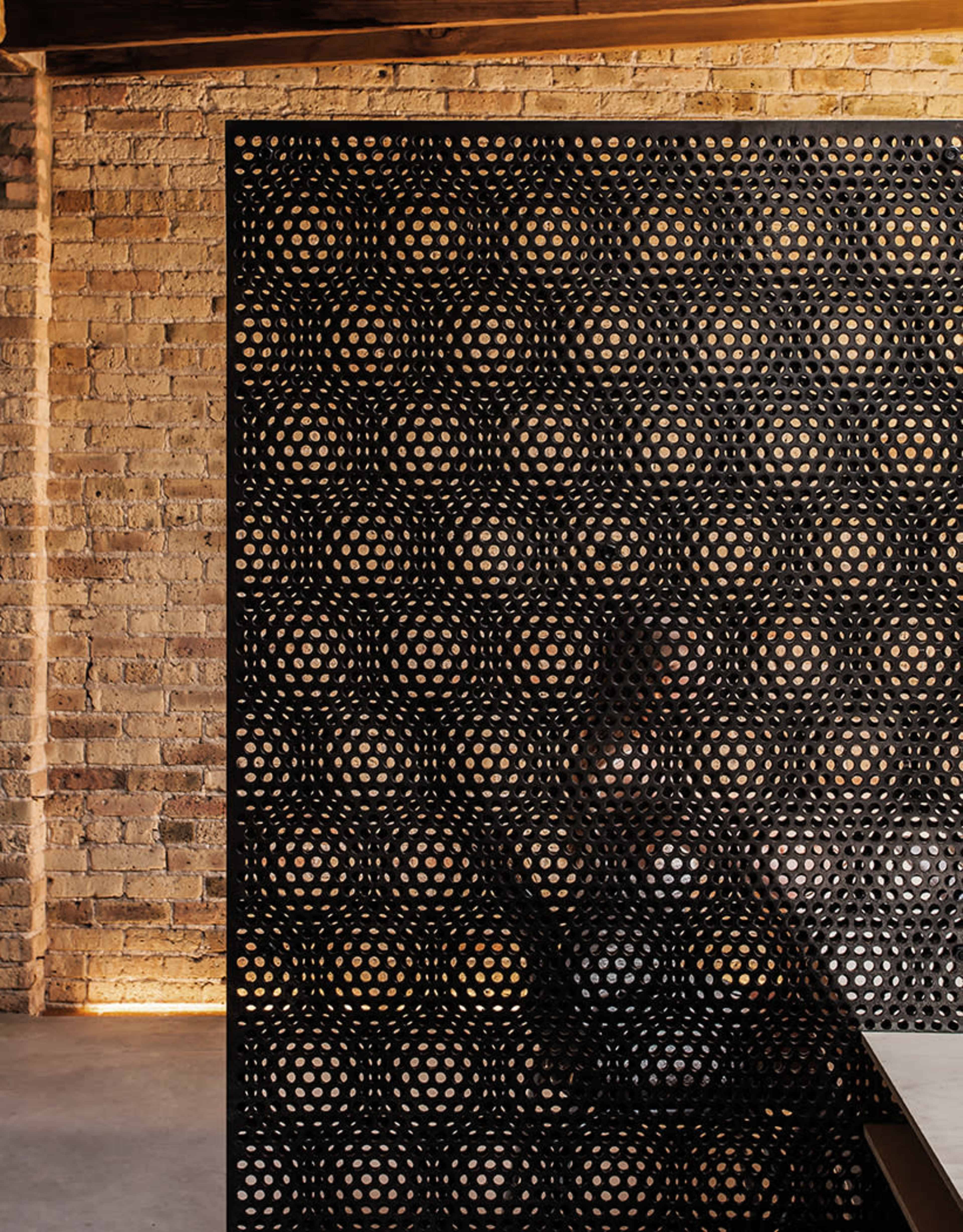 The image shows a perforated black screen against a backdrop of a textured brick wall.