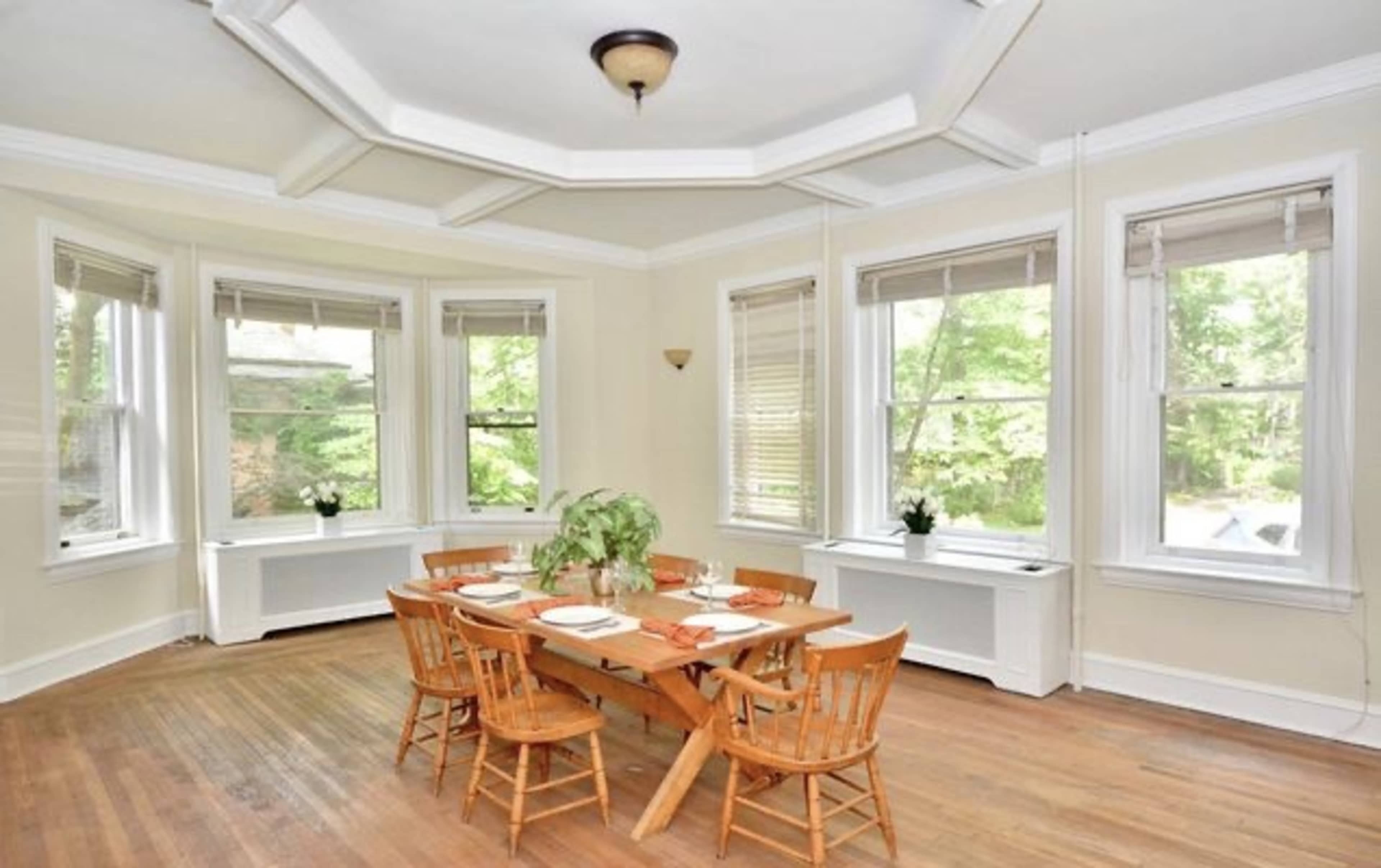 A dining room features a wooden table surrounded by six chairs and large windows allowing natural light to fill the space.