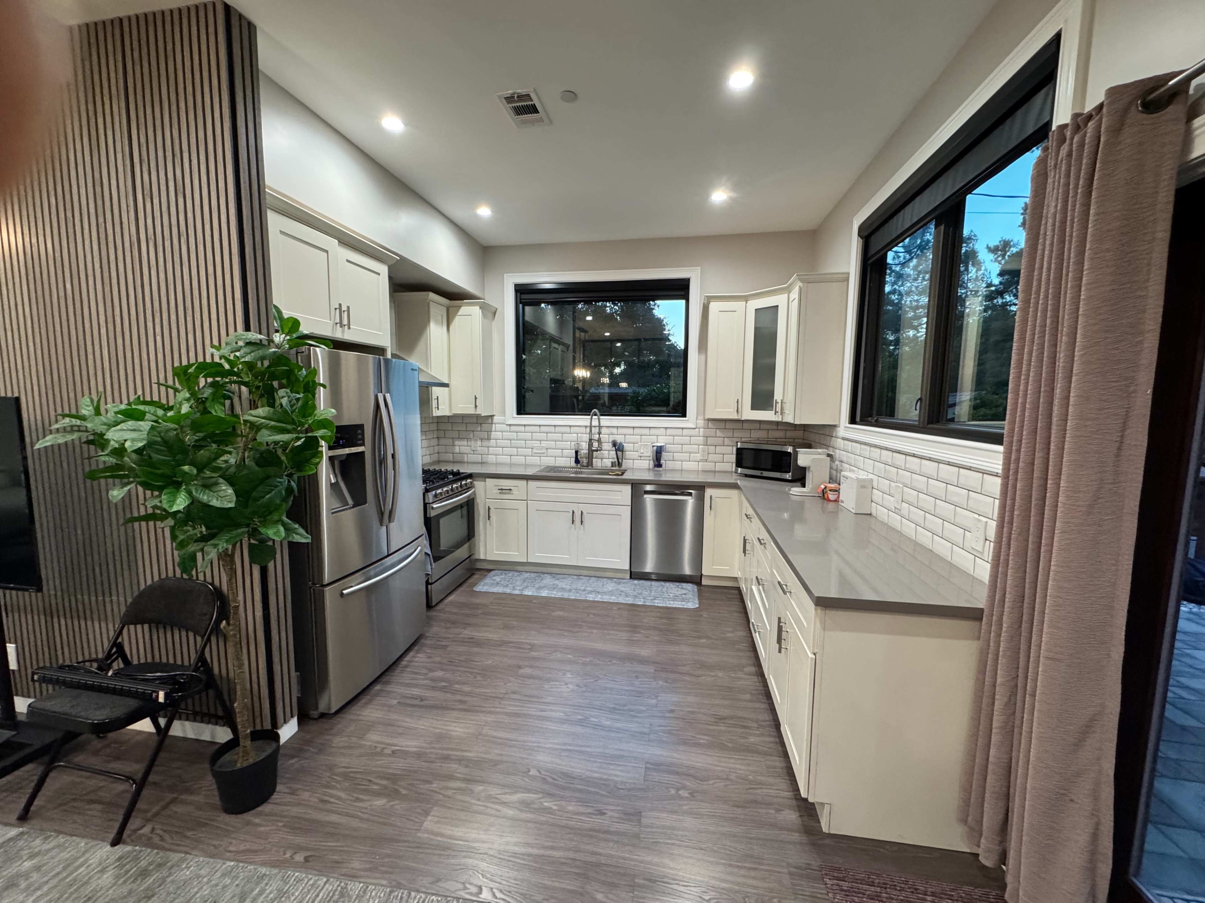 The kitchen features modern cabinetry, stainless steel appliances, and a large window overlooking the outside.