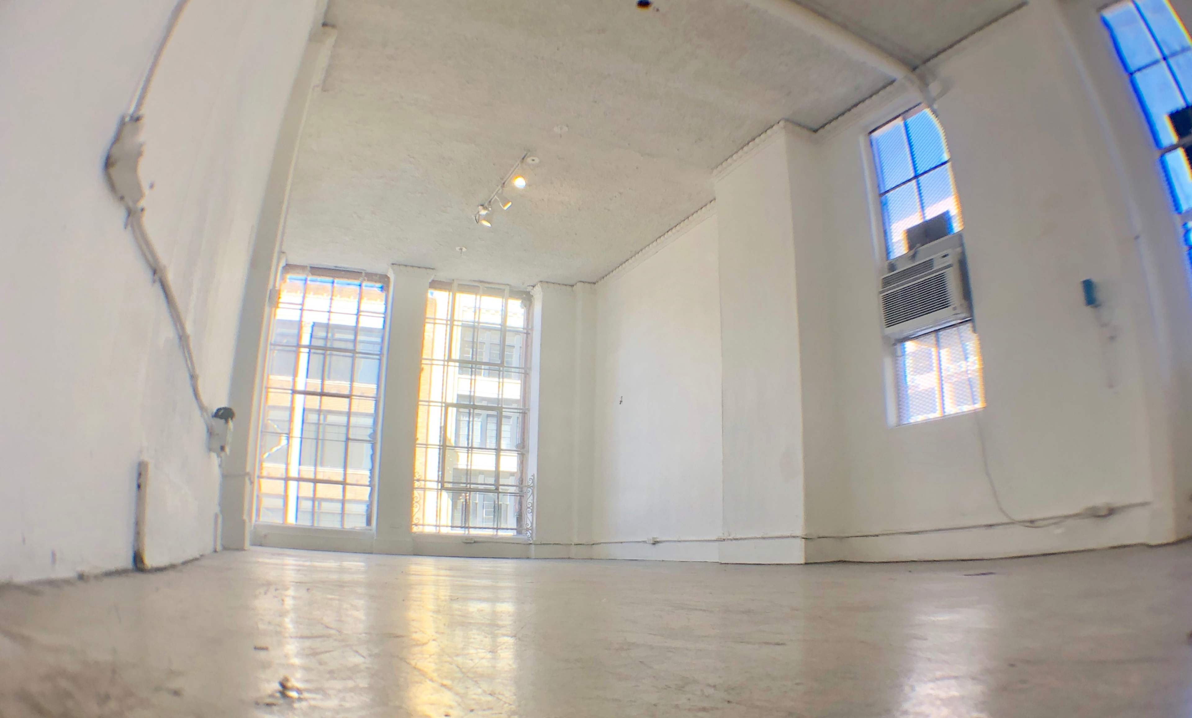 A vacant room with white walls, large windows, and a polished concrete floor.
