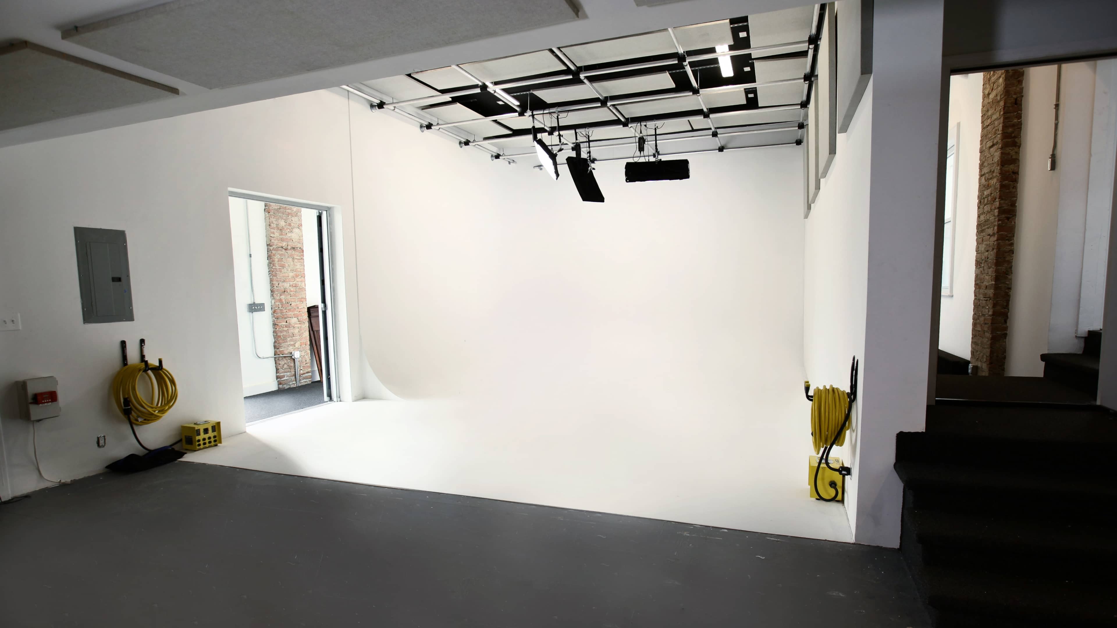 A blank, white studio space with industrial lighting and yellow cables on the floor.