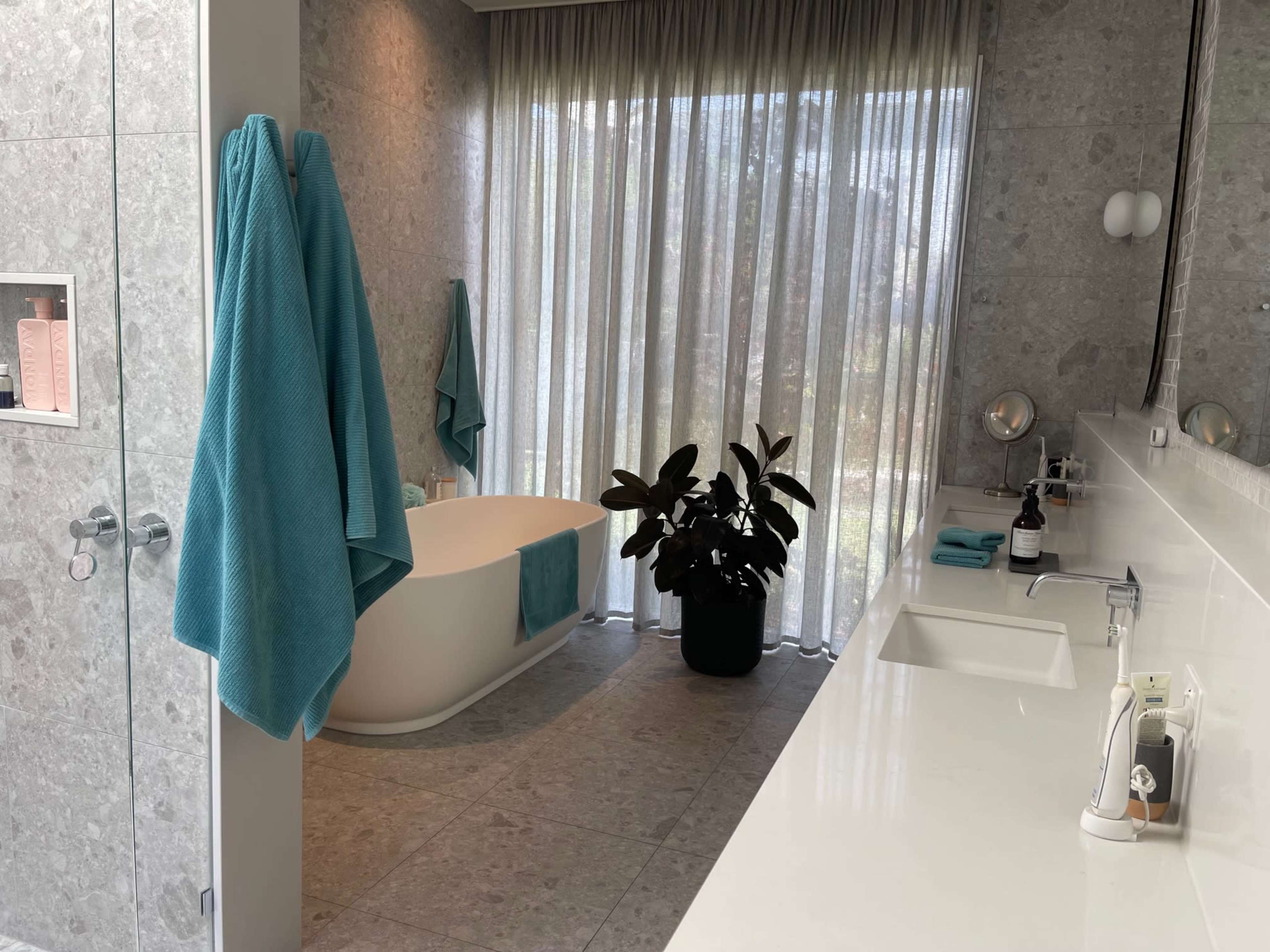 A modern bathroom featuring a freestanding tub, a plant in a black pot, and light blue towels hanging on the wall.