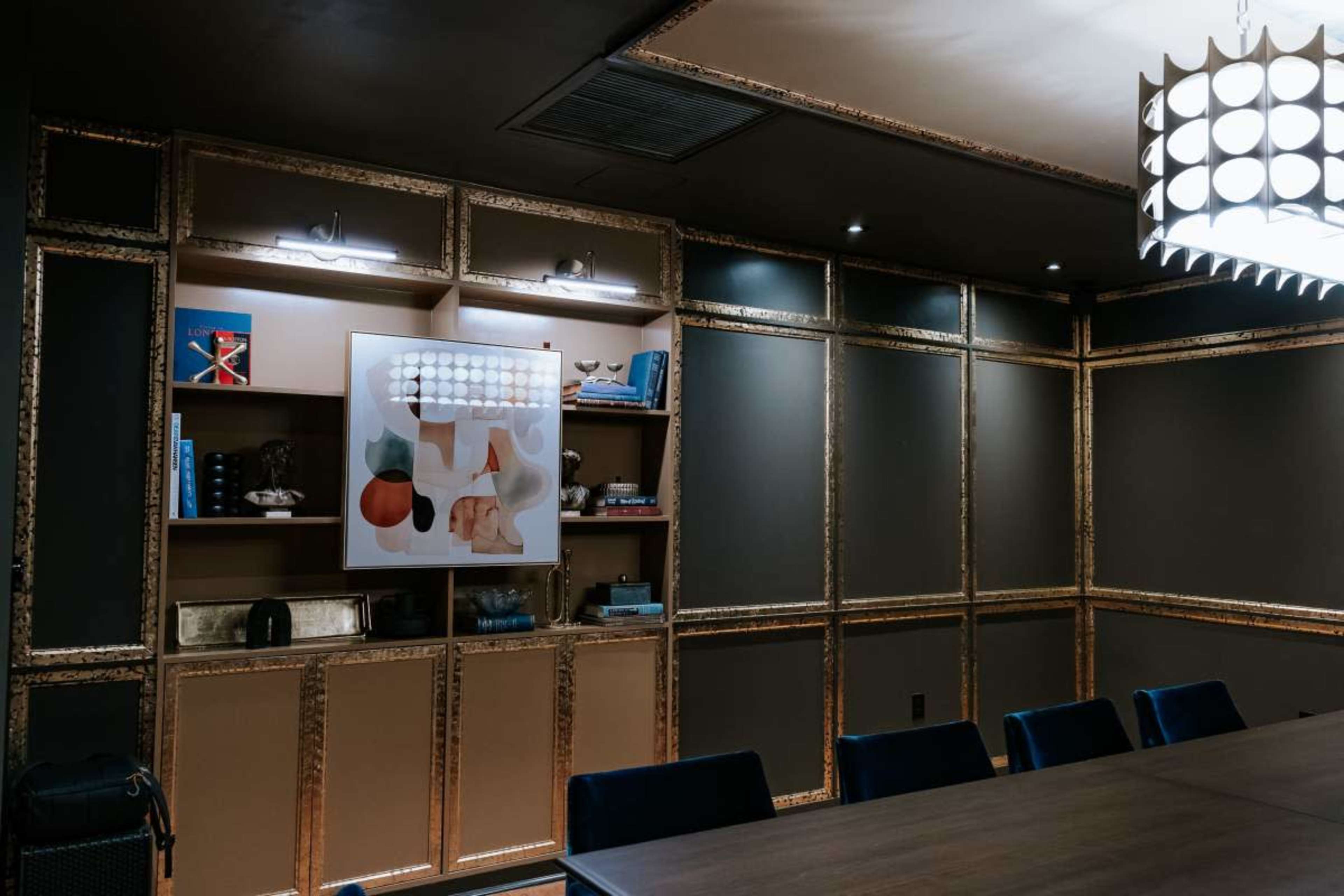 The image shows a modern conference room with a decorative wall unit featuring shelves, a large artwork, and a long table with blue chairs.
