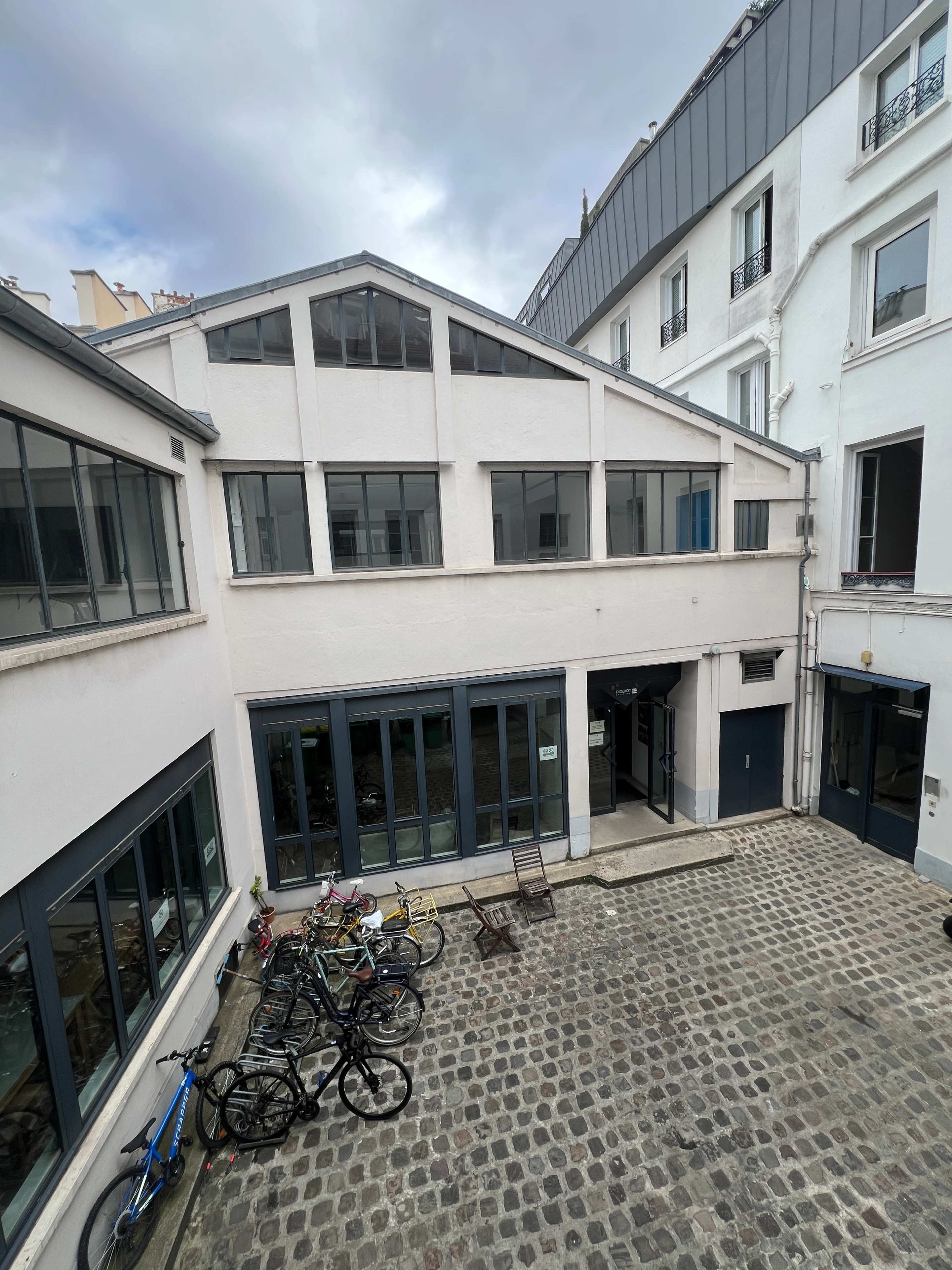 A cobblestone courtyard surrounded by white buildings with large windows and several parked bicycles.