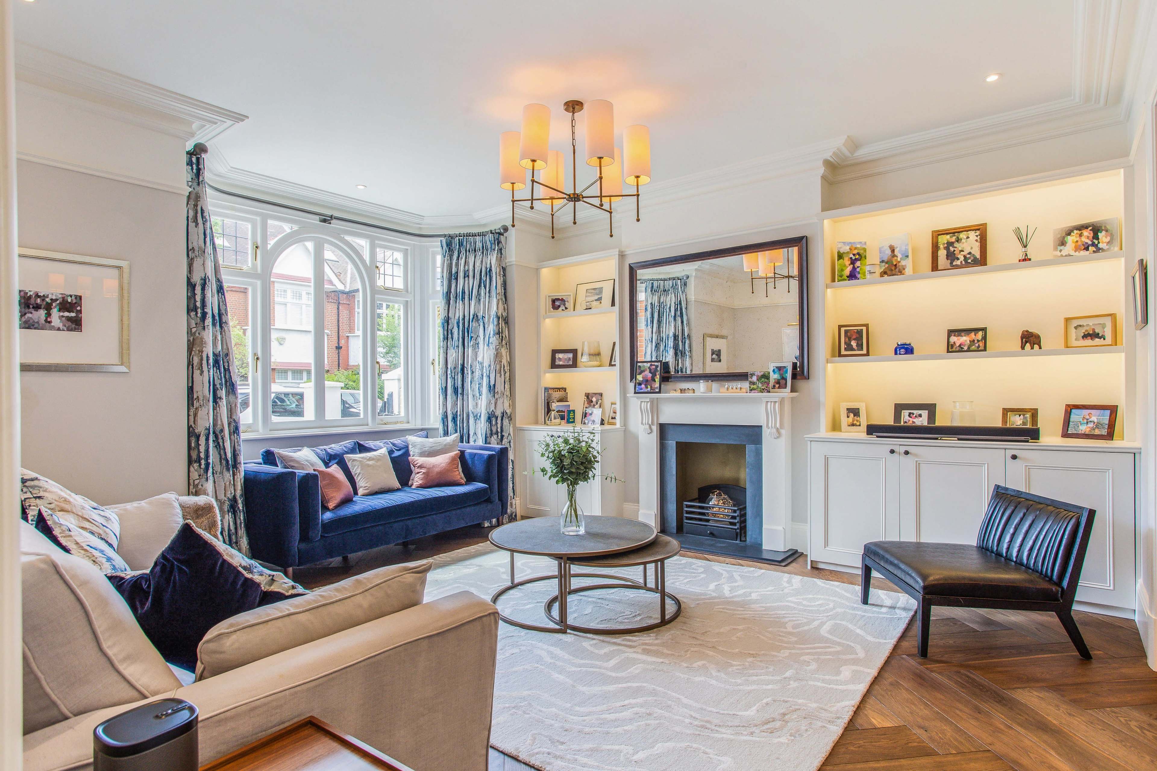 The living room features a blue sofa, a round coffee table, and a fireplace, all arranged around a large window and surrounded by decorative shelving.