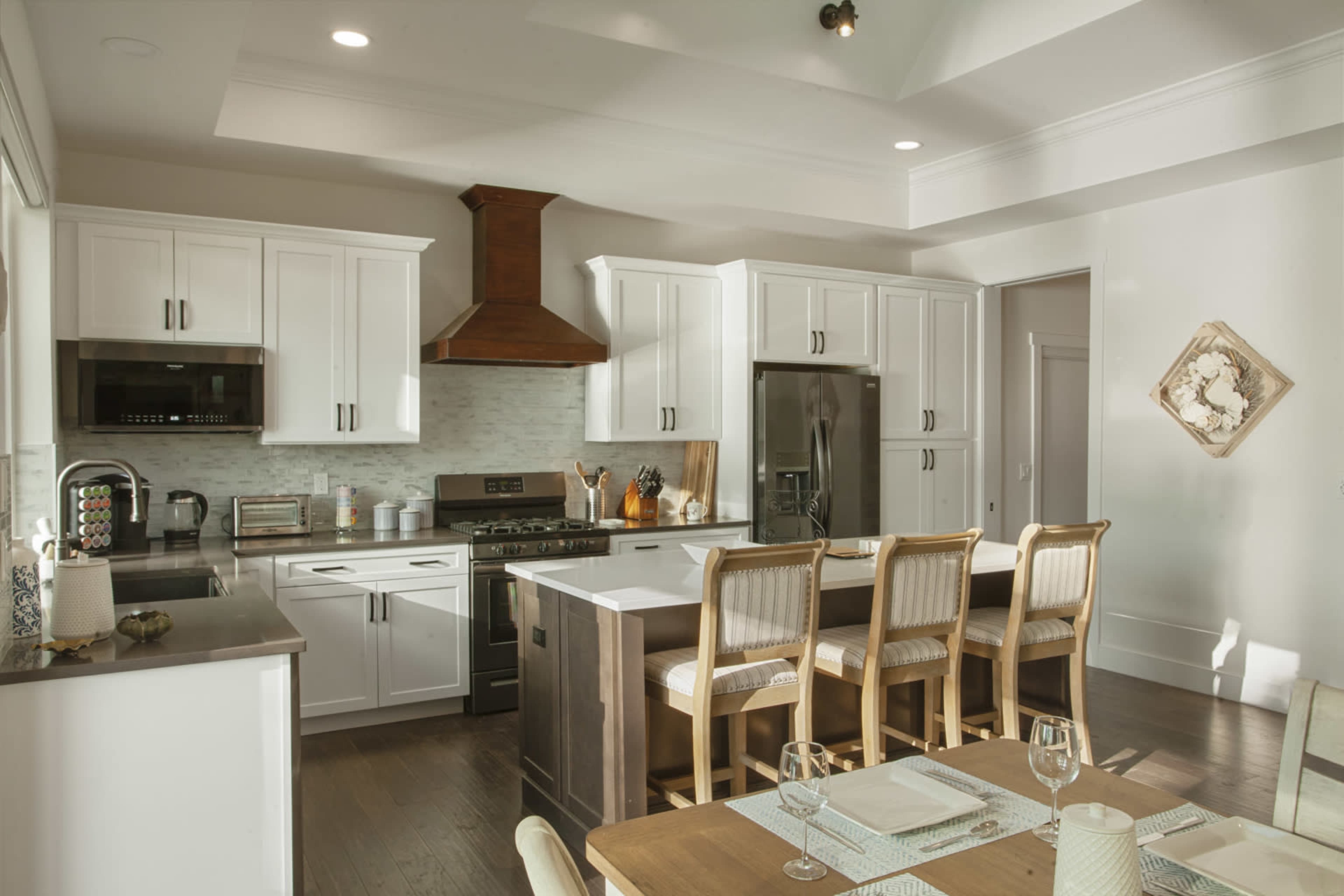 A modern kitchen with white cabinets, stainless steel appliances, and a wooden dining table set for a meal.