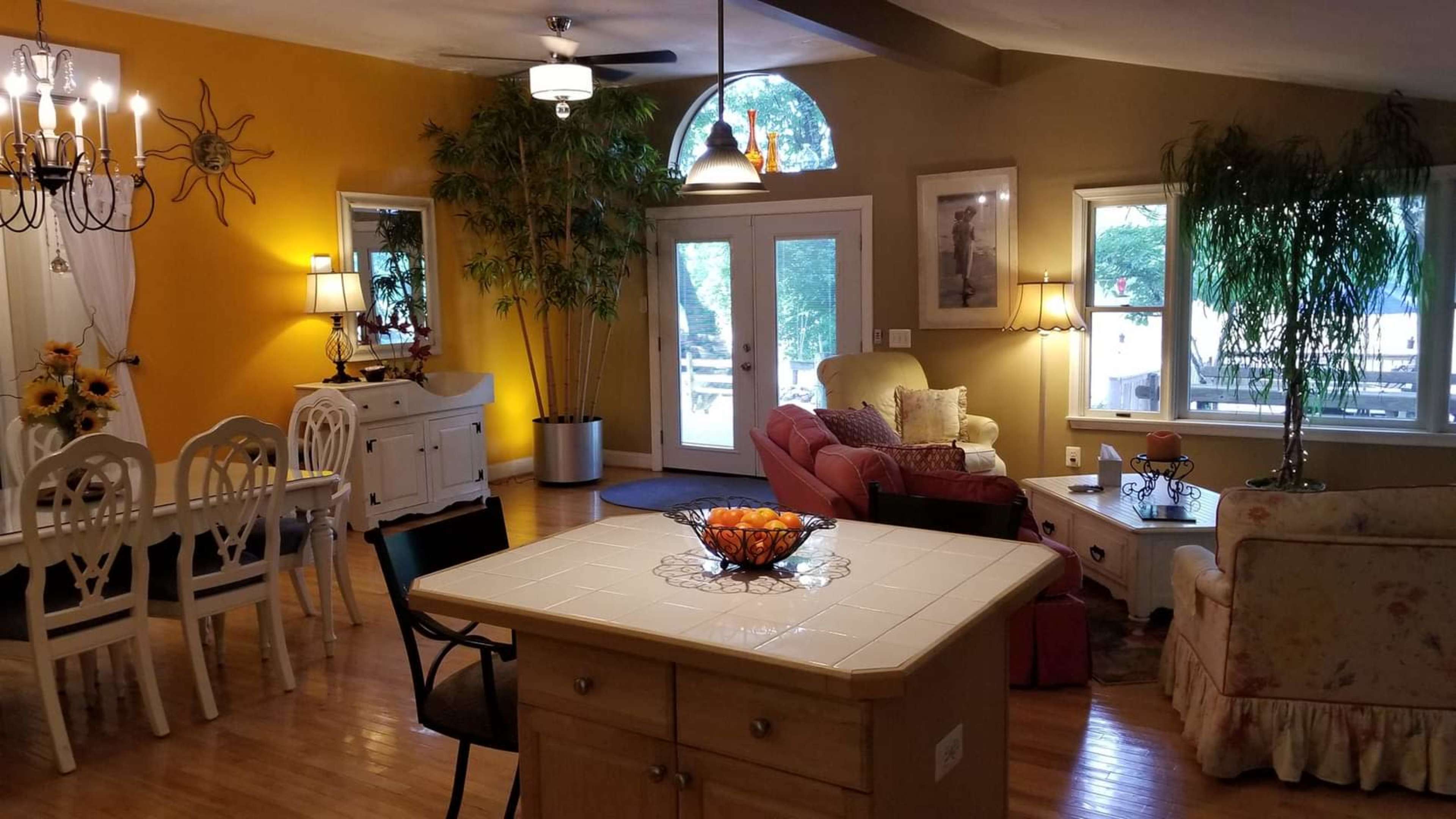 A spacious living area features a dining table, two seating areas, and large windows providing natural light.