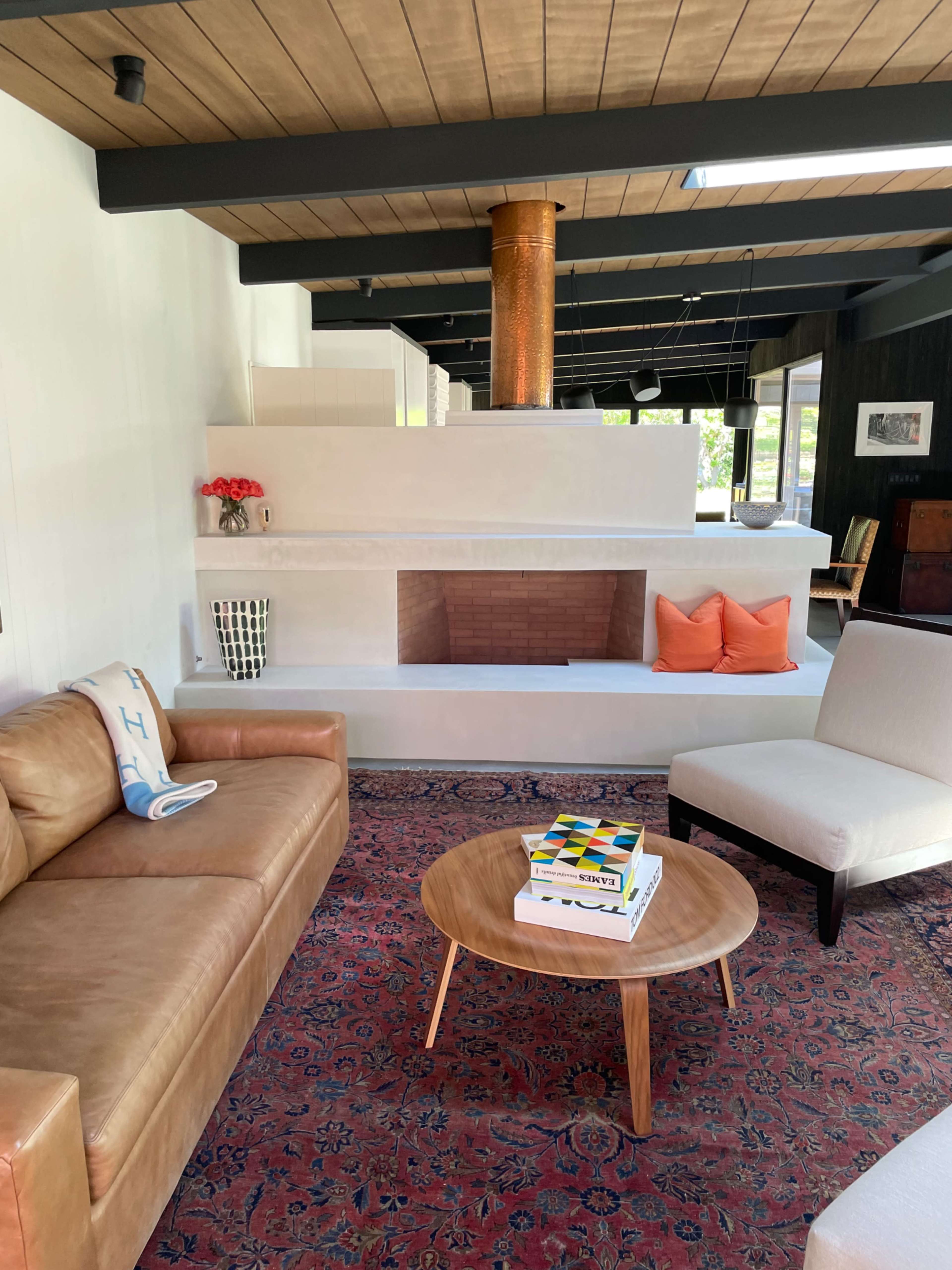 A modern living room with a leather sofa, an armchair, a round wooden coffee table, and a prominent fireplace featuring a copper flue.