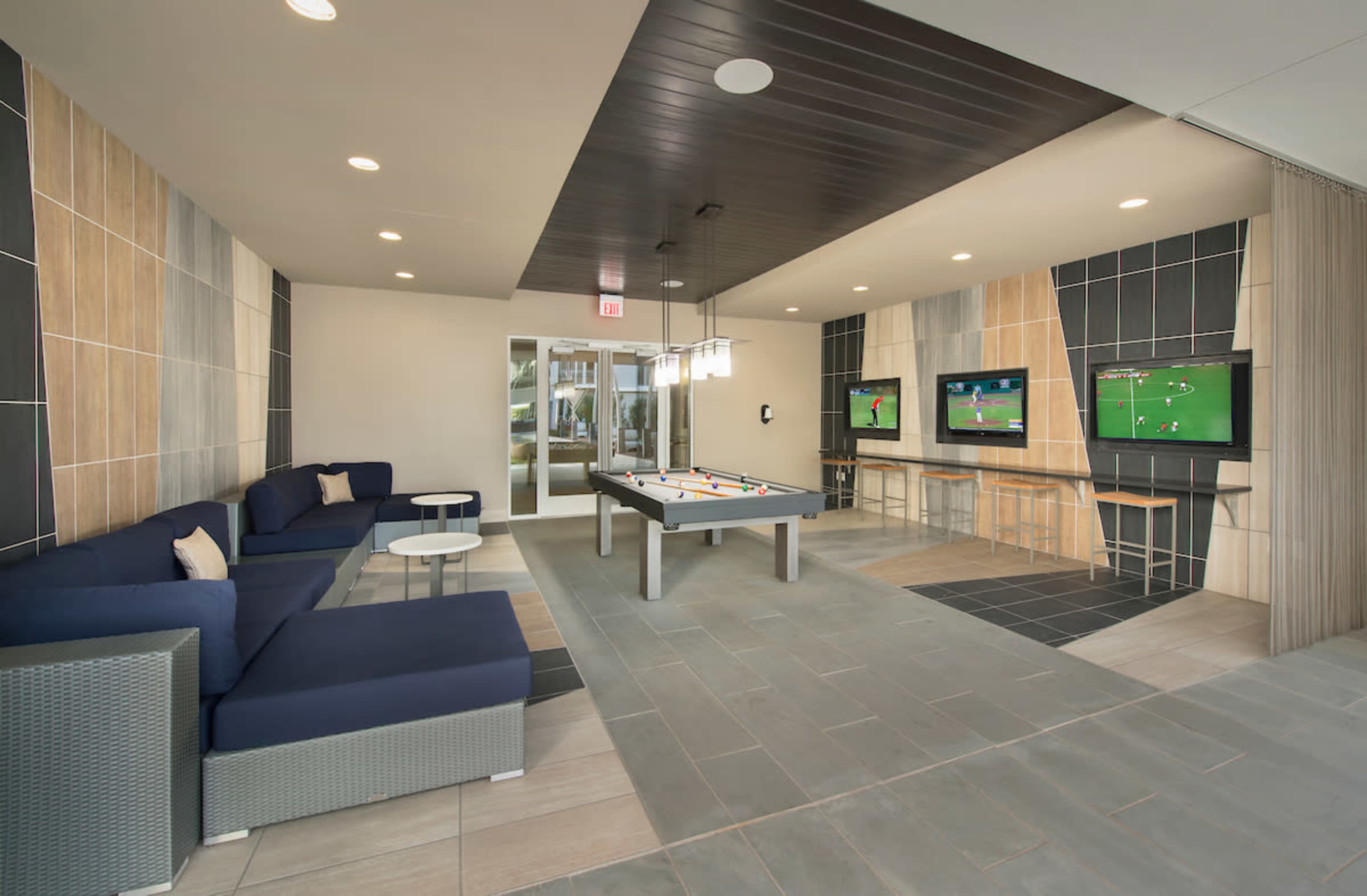 A modern lounge area featuring a pool table and two televisions mounted on the wall, surrounded by seating.