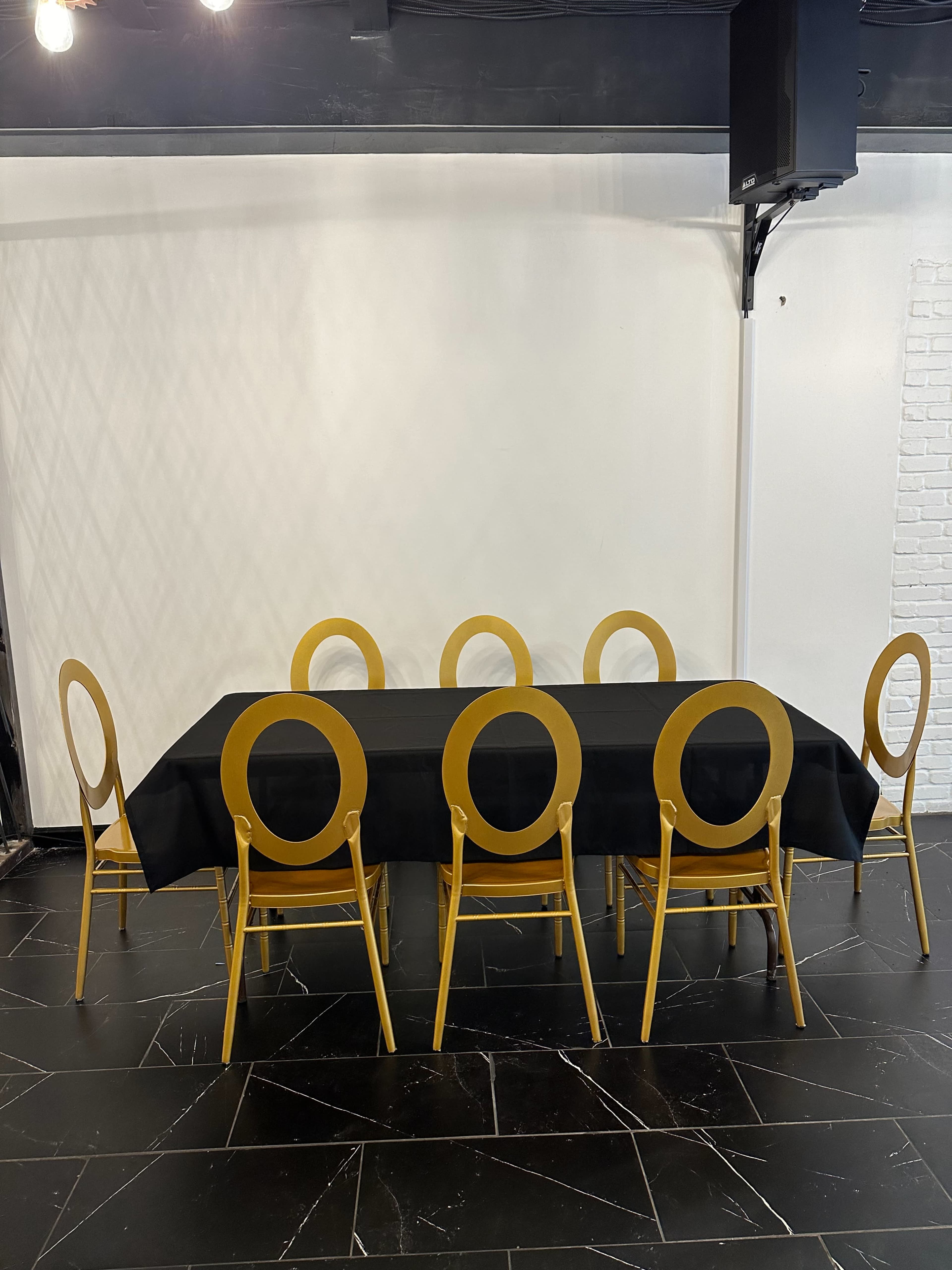 A black table is set with six gold chairs arranged around it in a minimalist room.