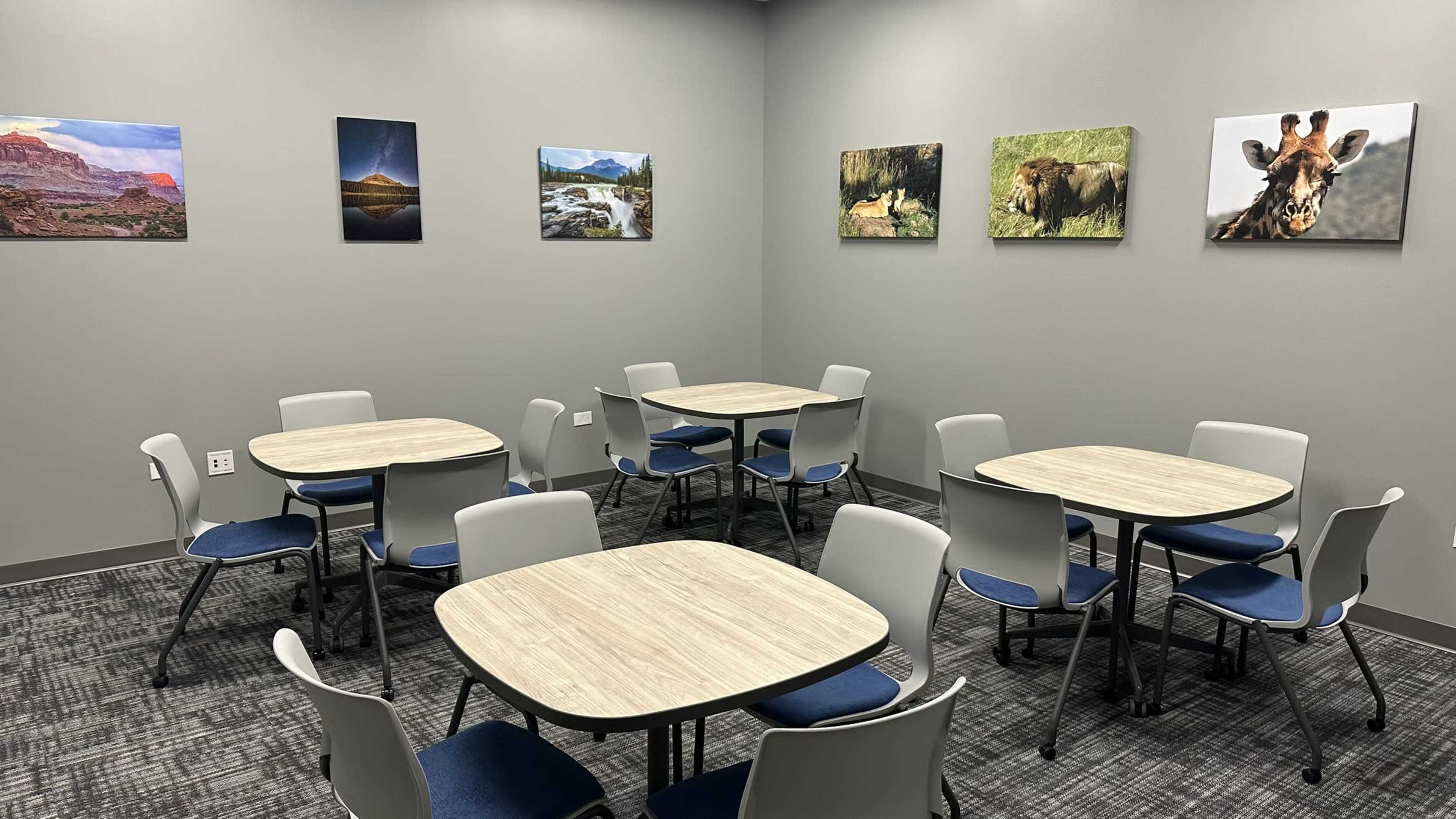 The image shows a meeting room with several tables and chairs arranged in a symmetrical layout, featuring framed nature and animal photographs on the walls.