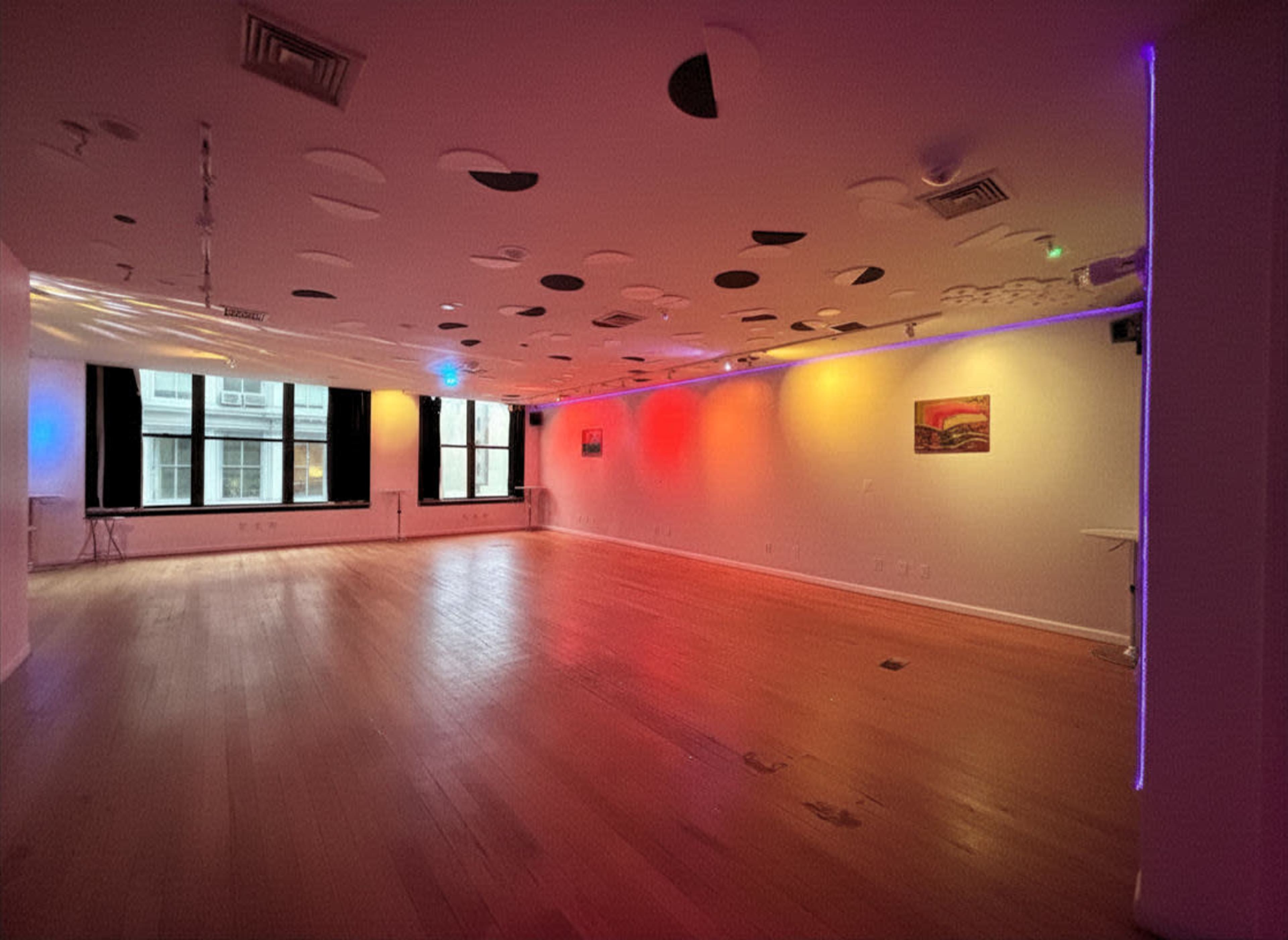 The image shows a spacious interior room with wooden flooring, colorful lighting, and abstract ceiling decorations.