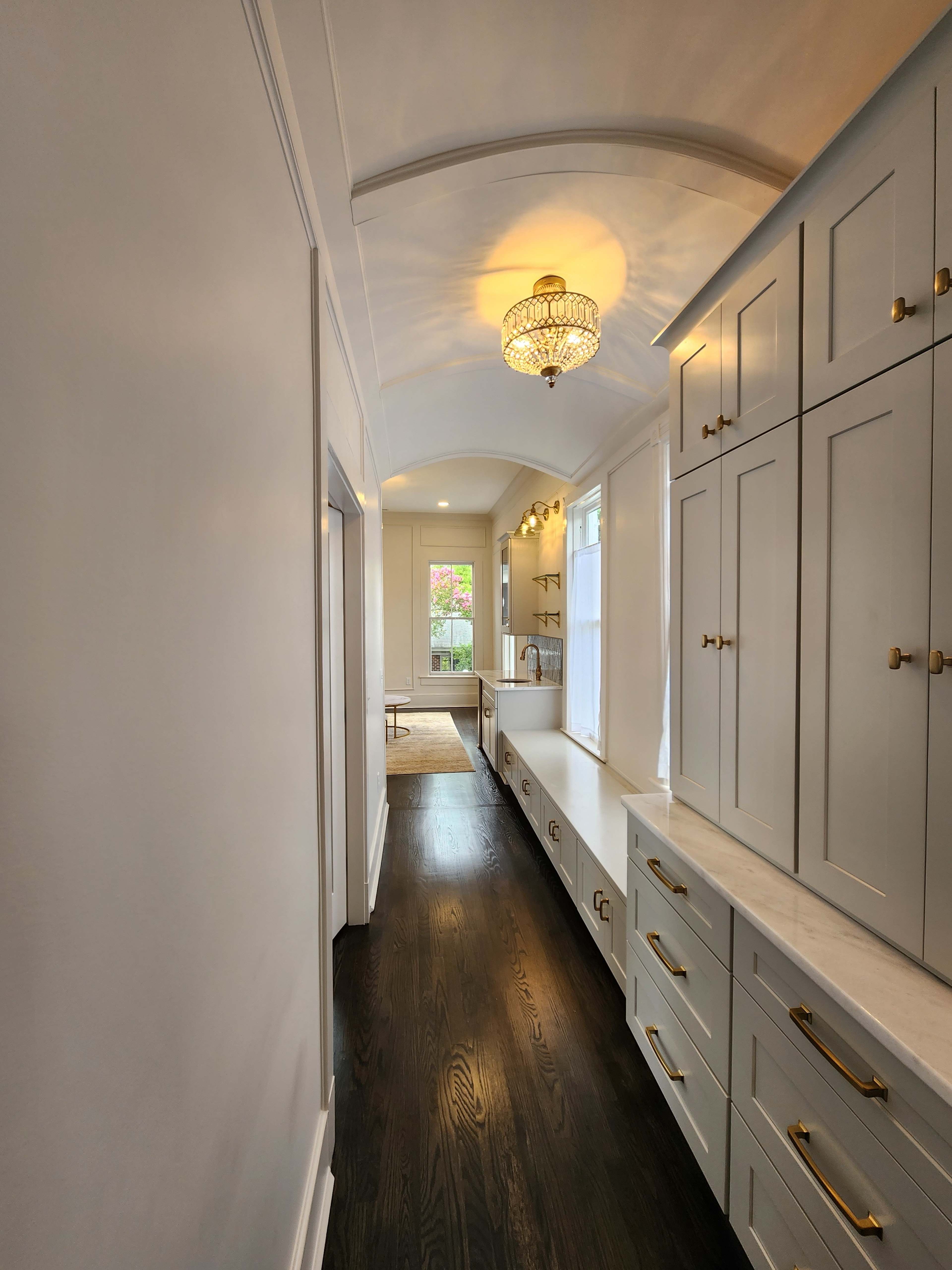 A long hallway with dark wooden flooring, gray cabinetry, and a chandelier illuminates the space.