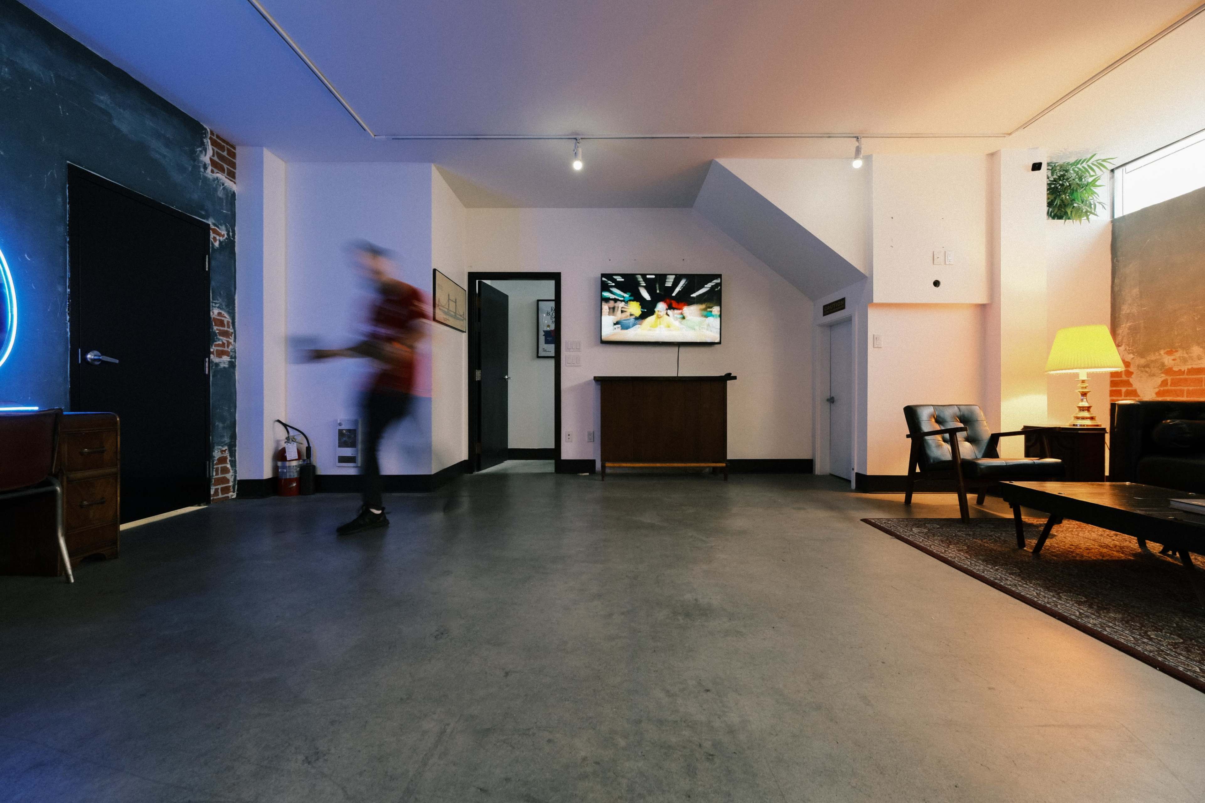 A spacious room features a television on the wall, a wooden cabinet, and a seating area with a couch and chair.