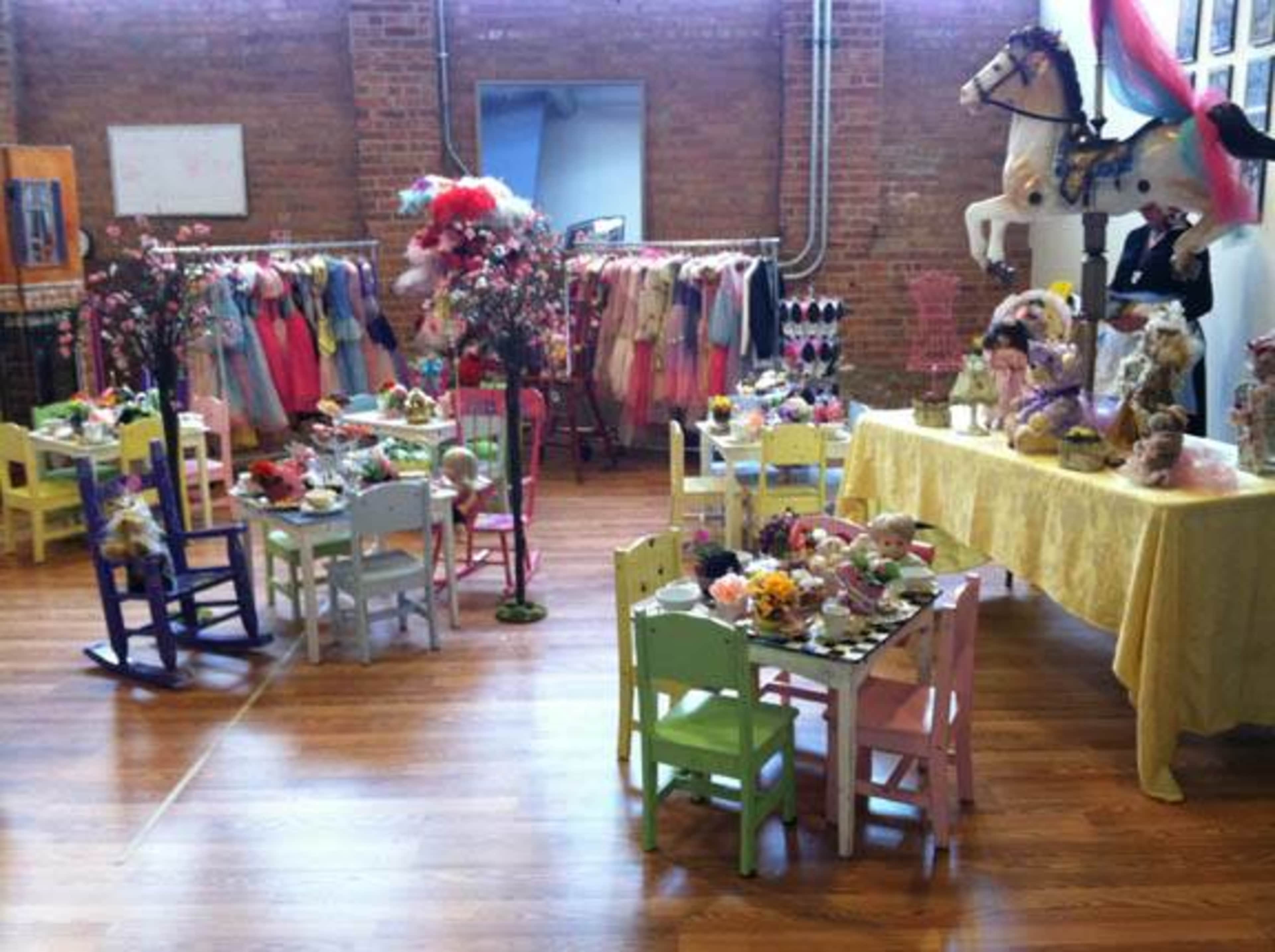 The scene features a brightly decorated children's playroom with colorful furniture, a dress rack filled with costumes, and a table set for tea with dolls and floral arrangements.