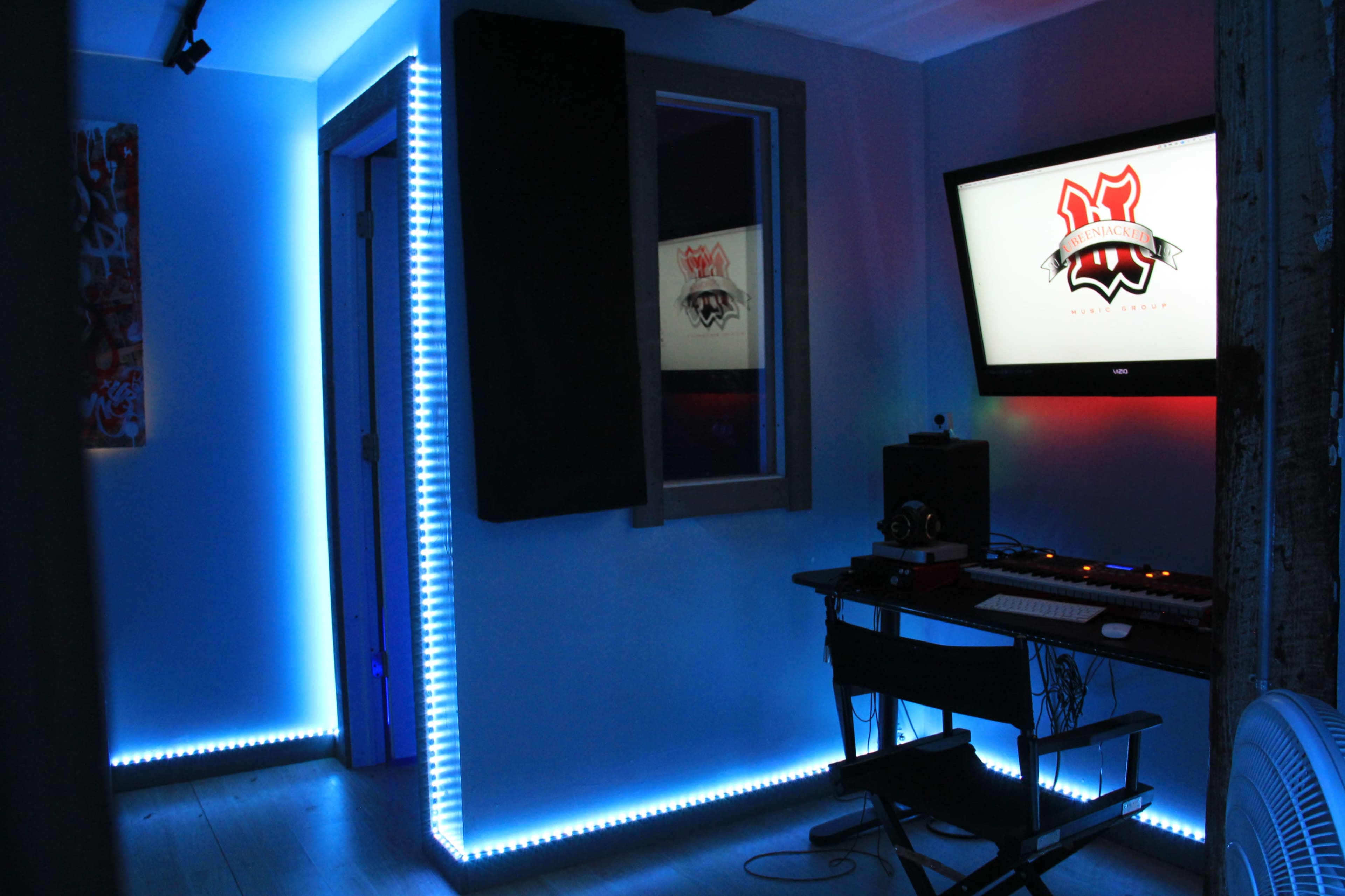 A modern studio space features a desk with a computer and keyboard, illuminated by blue LED lights along the walls and floor.