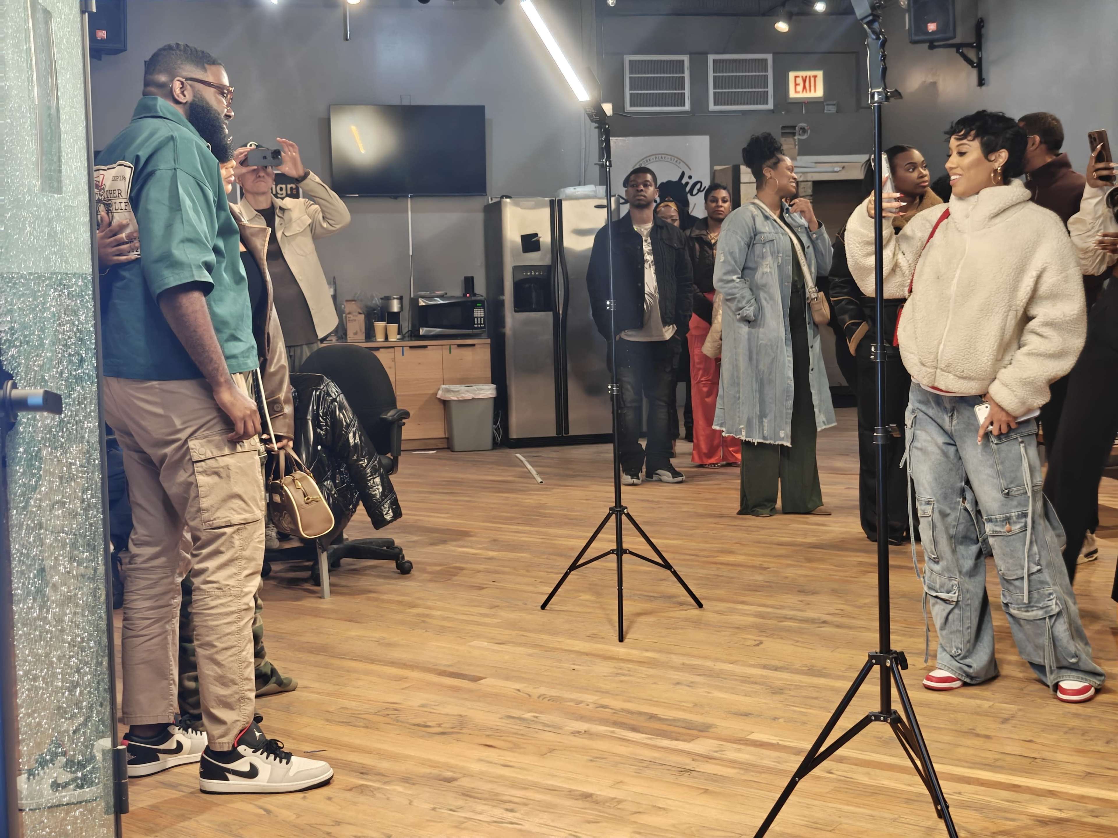 A group of people is gathered in a spacious room, with one individual posing for a photo while others observe and take pictures.