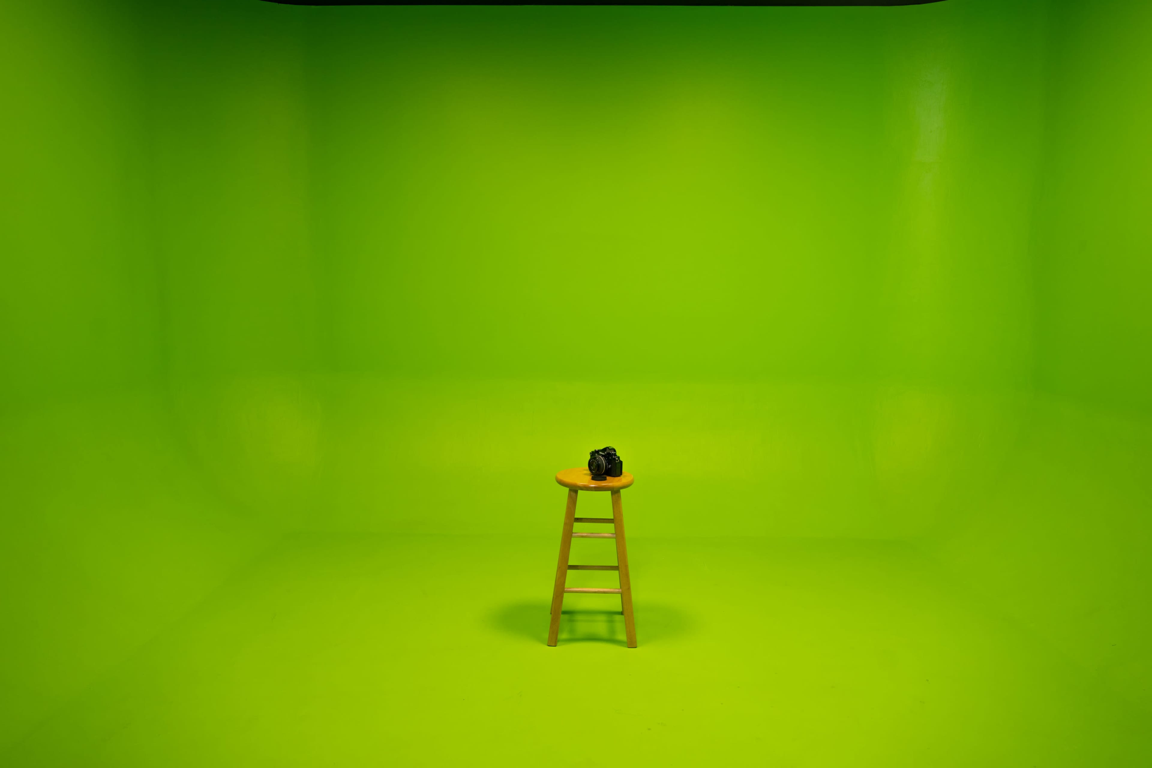 A wooden stool with a camera sits in the center of an empty green room.