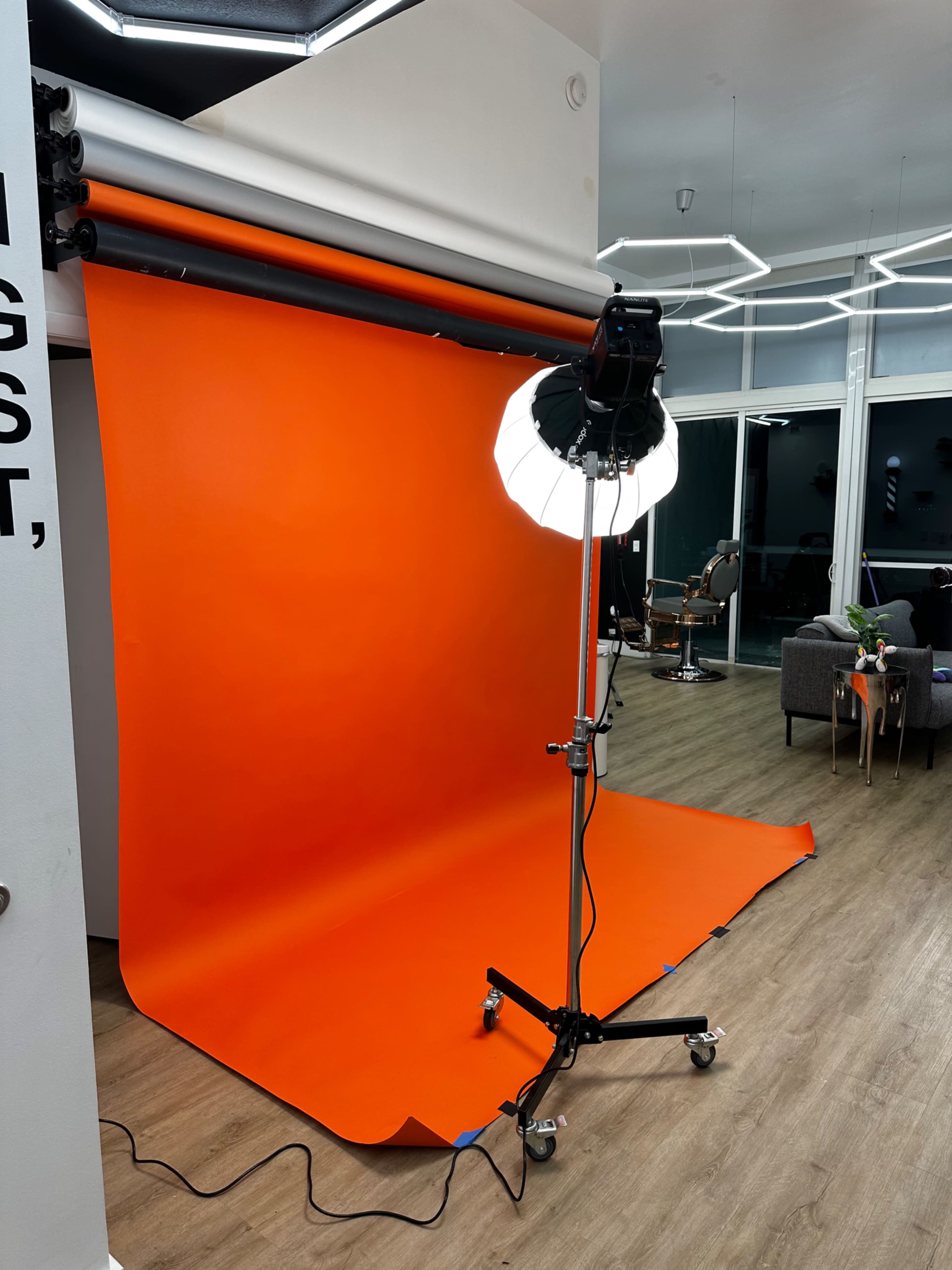 A photography studio with an orange backdrop, a lighting setup on a stand, and modern furnishings in the background.