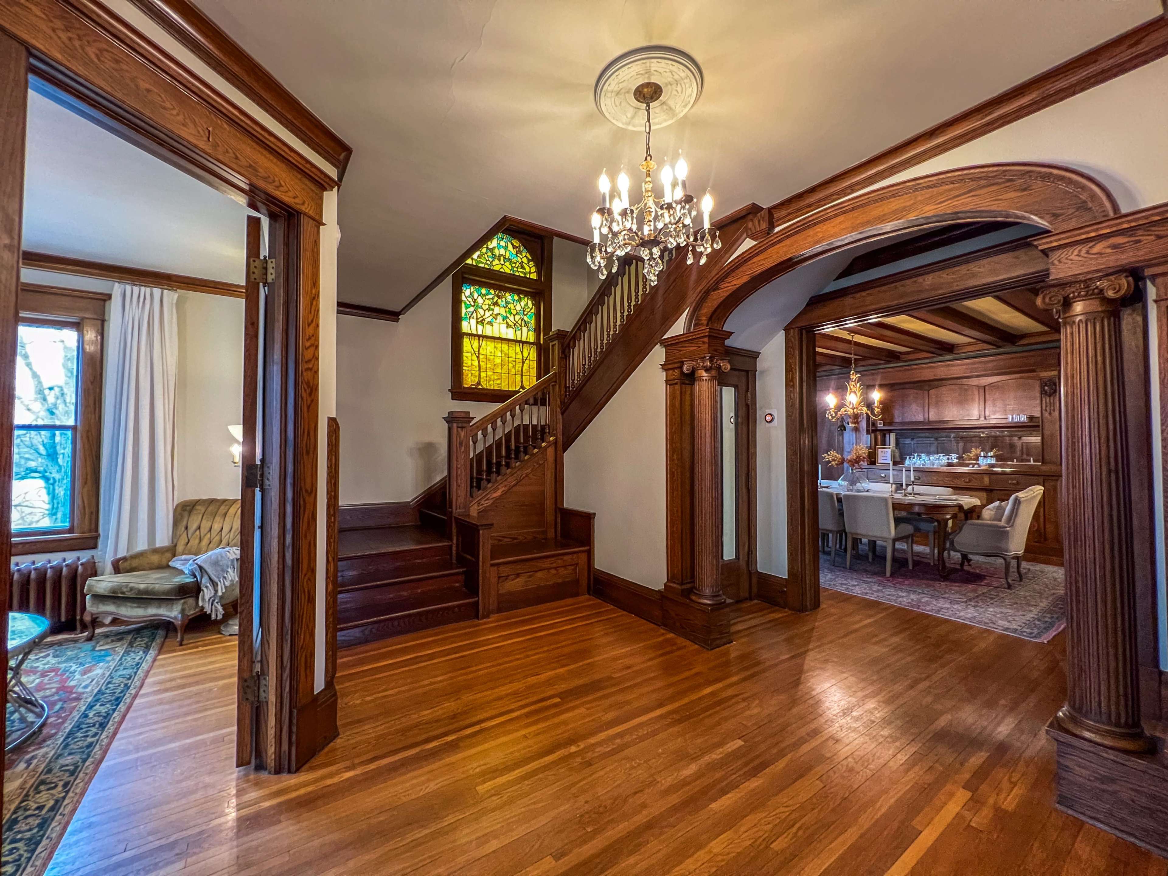 An entryway of a vintage home featuring a staircase, ornate woodwork, and a stained glass window.