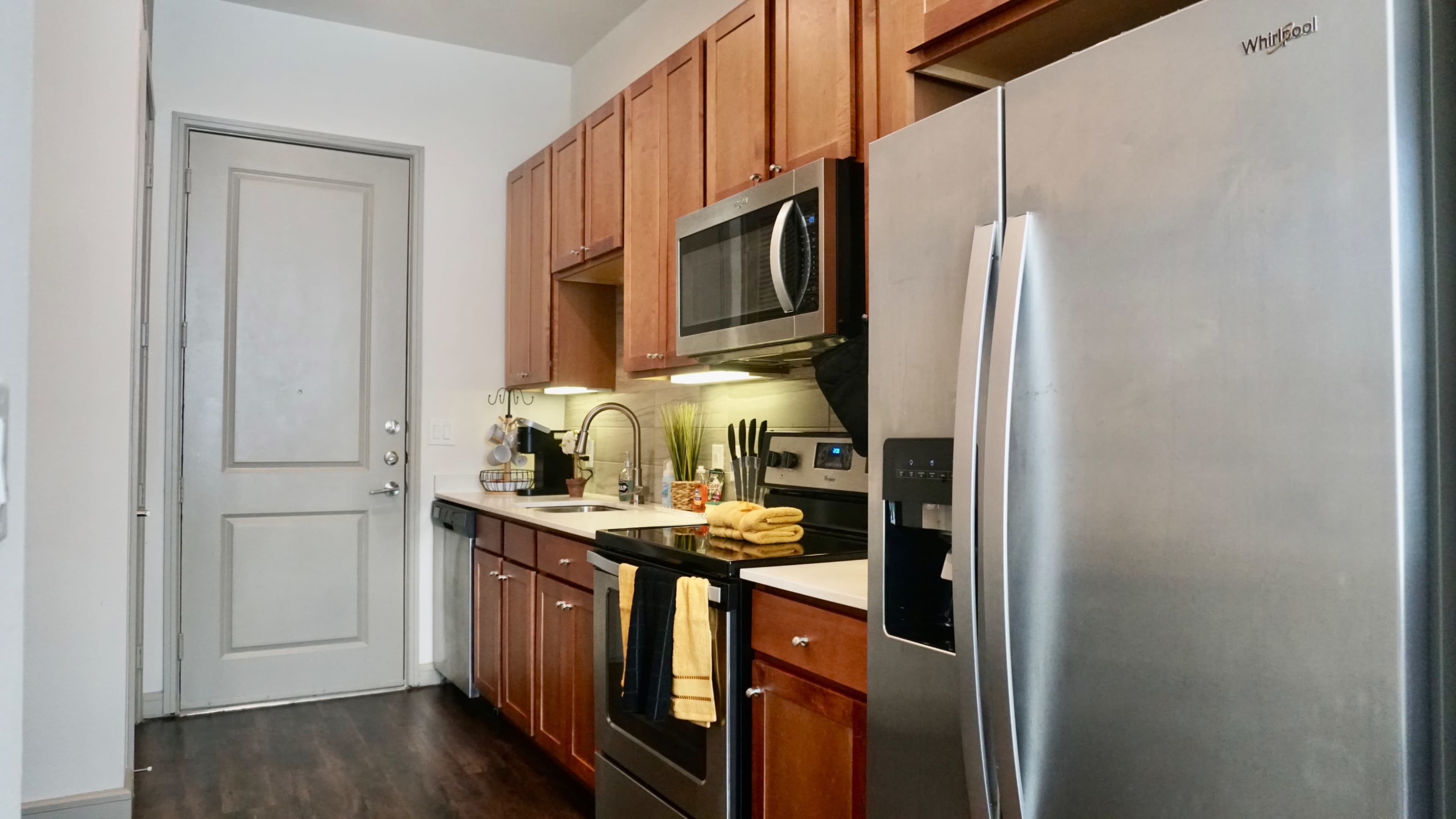 A compact kitchen with wooden cabinets, stainless steel appliances, and a countertop equipped with kitchen utensils and bright towels.