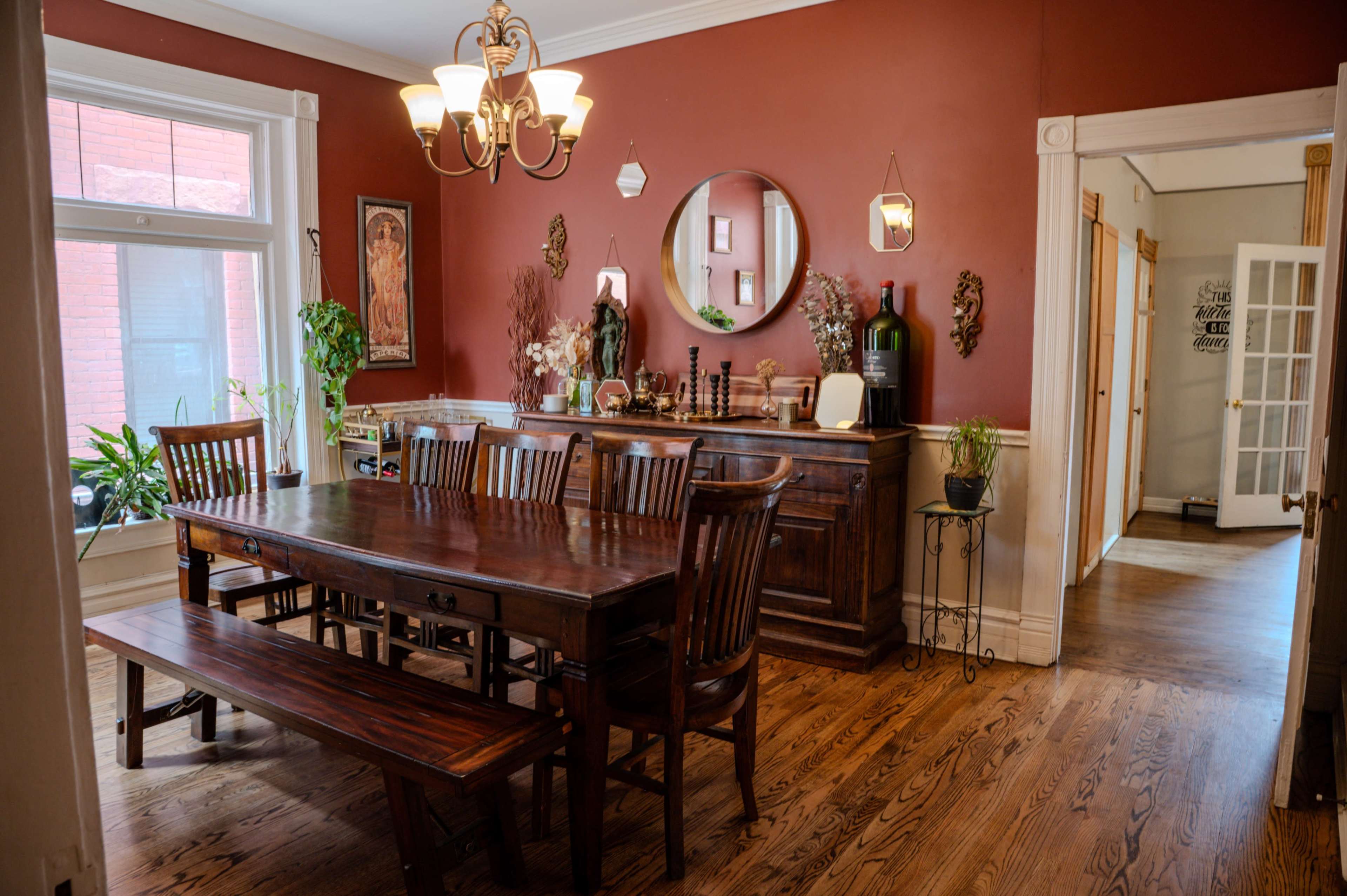 The image features a dining room with a large wooden table, several chairs, a sideboard, and warm-toned walls, adorned with decorative elements and plants.