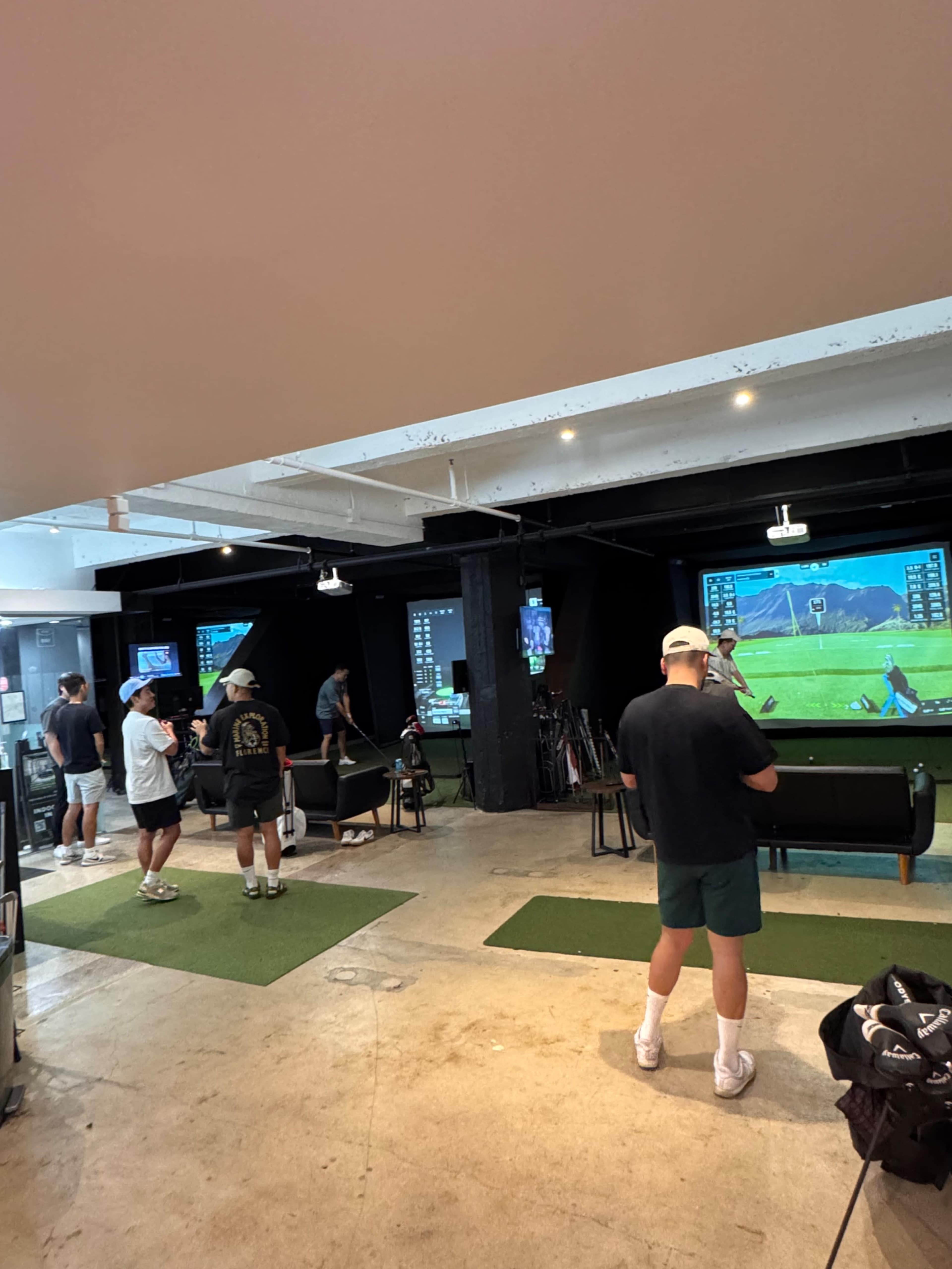 Several individuals are practicing their golf swings using simulators in an indoor golf facility.