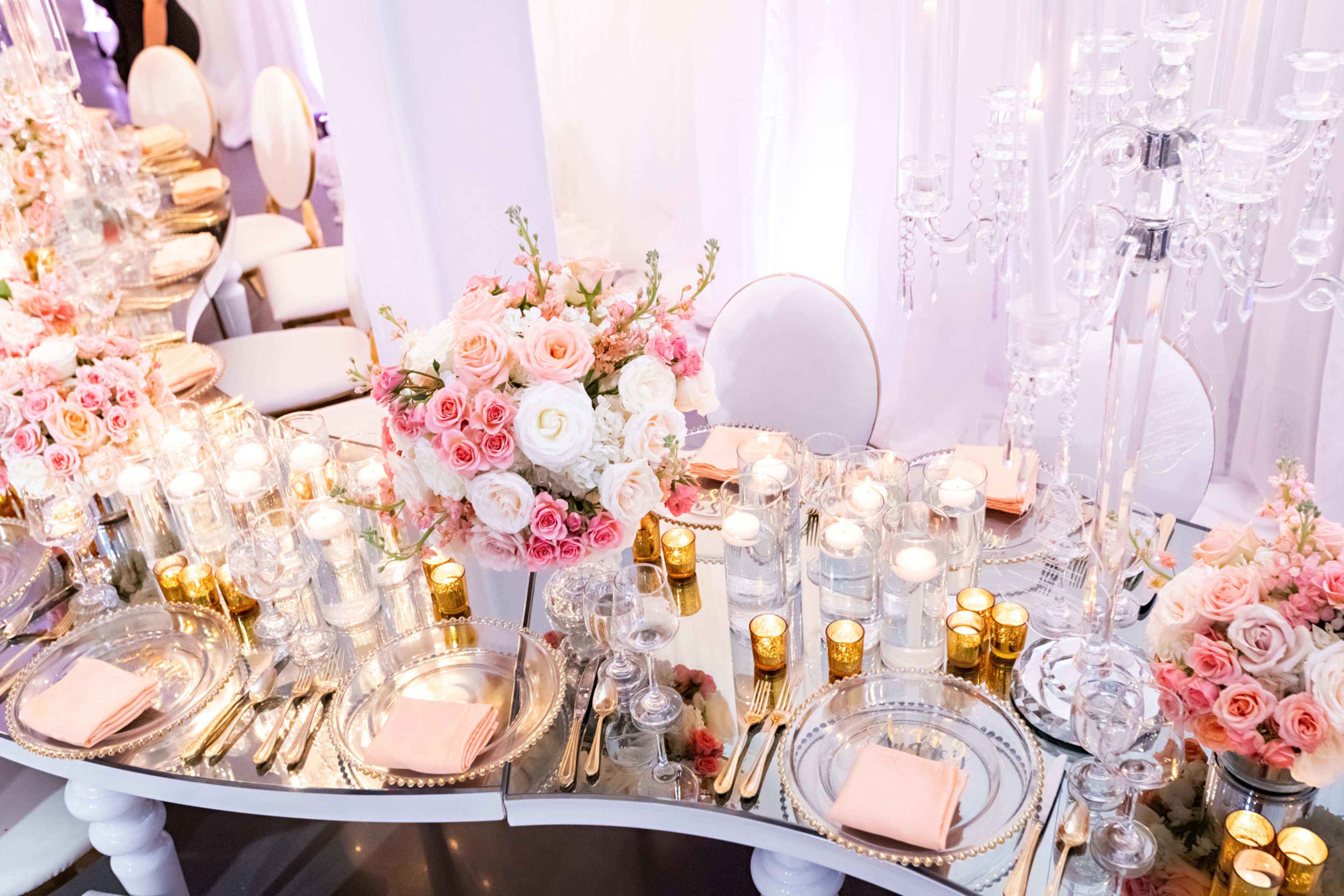 A beautifully arranged dining table features an elaborate floral centerpiece with roses, surrounded by candles and elegant tableware.
