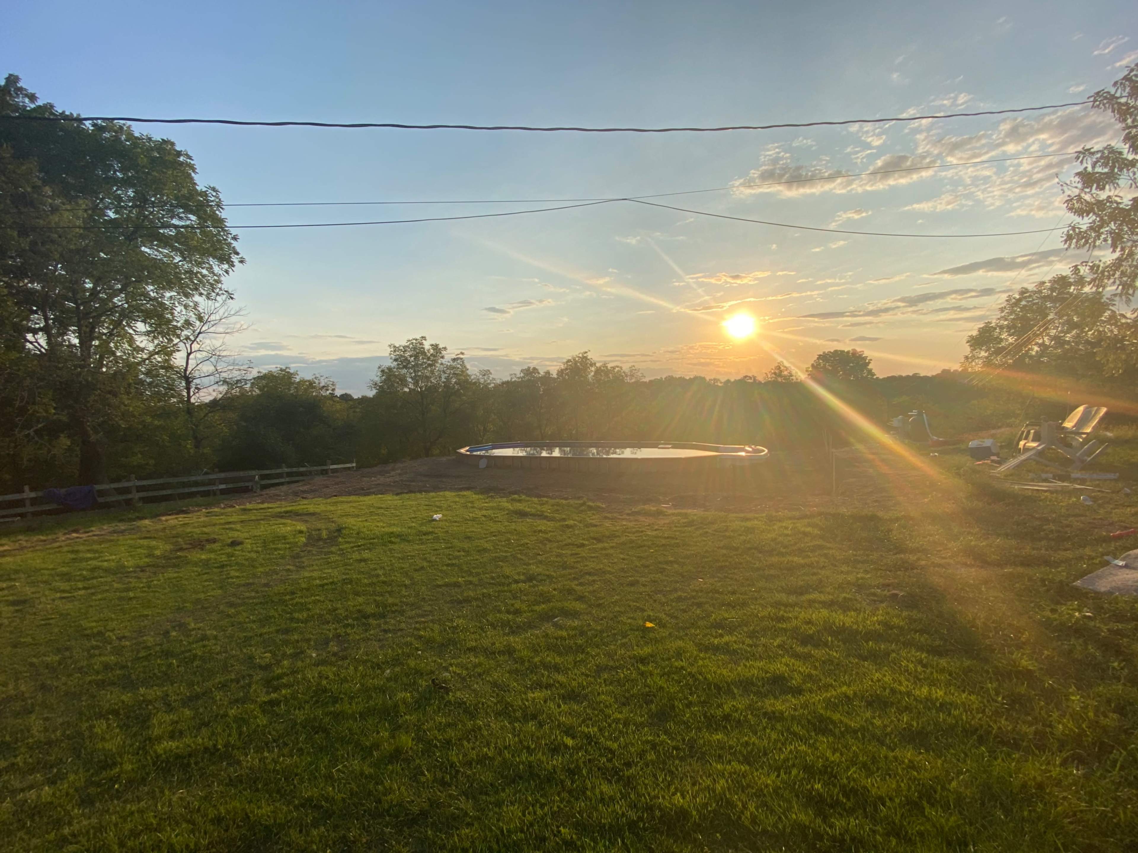 The scene shows a grassy area with a swimming pool and a sunset casting light across the landscape.