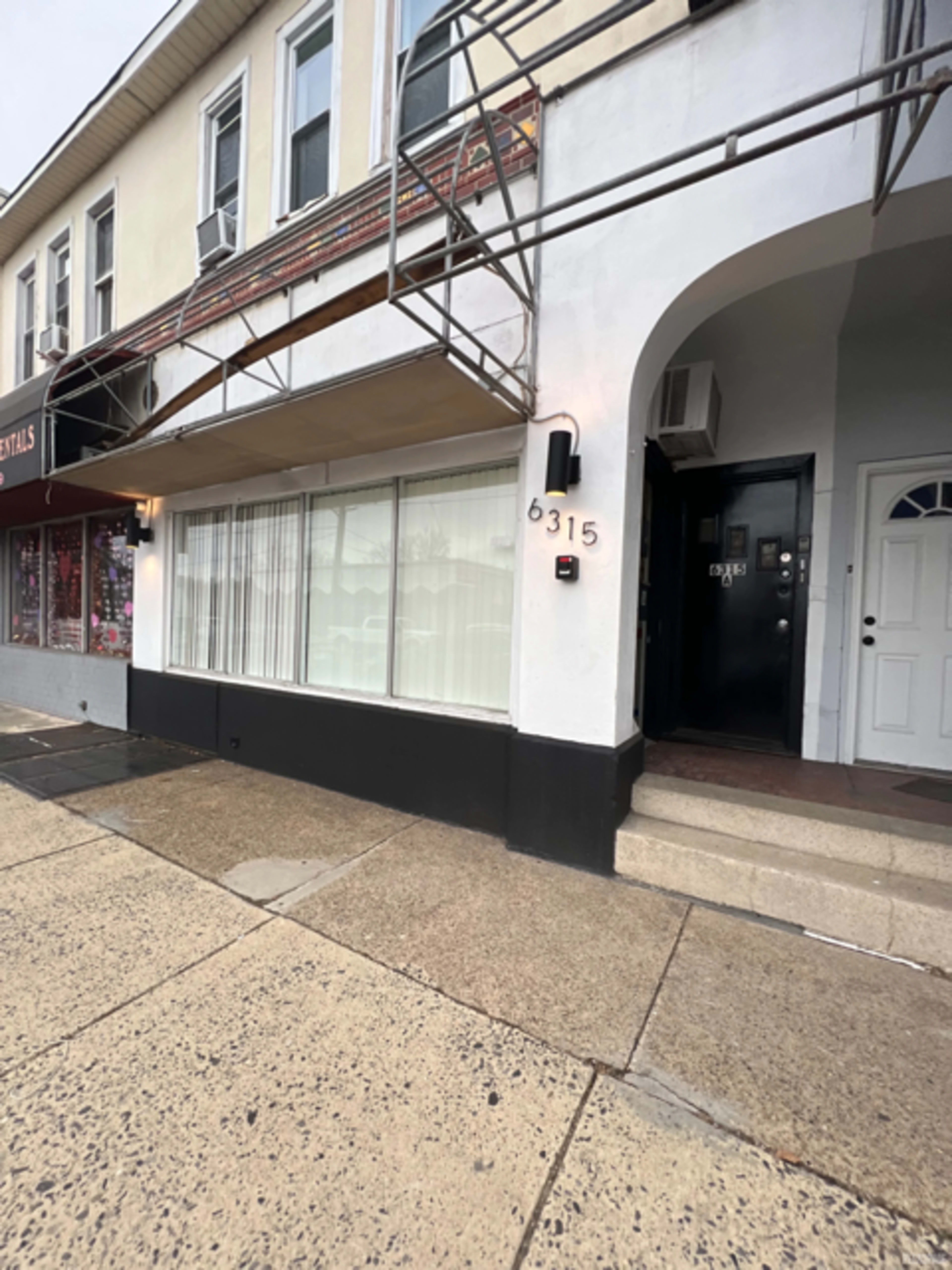 The image shows a building with a storefront featuring large windows, a black door, and scaffolding above the entrance, located at 6315.