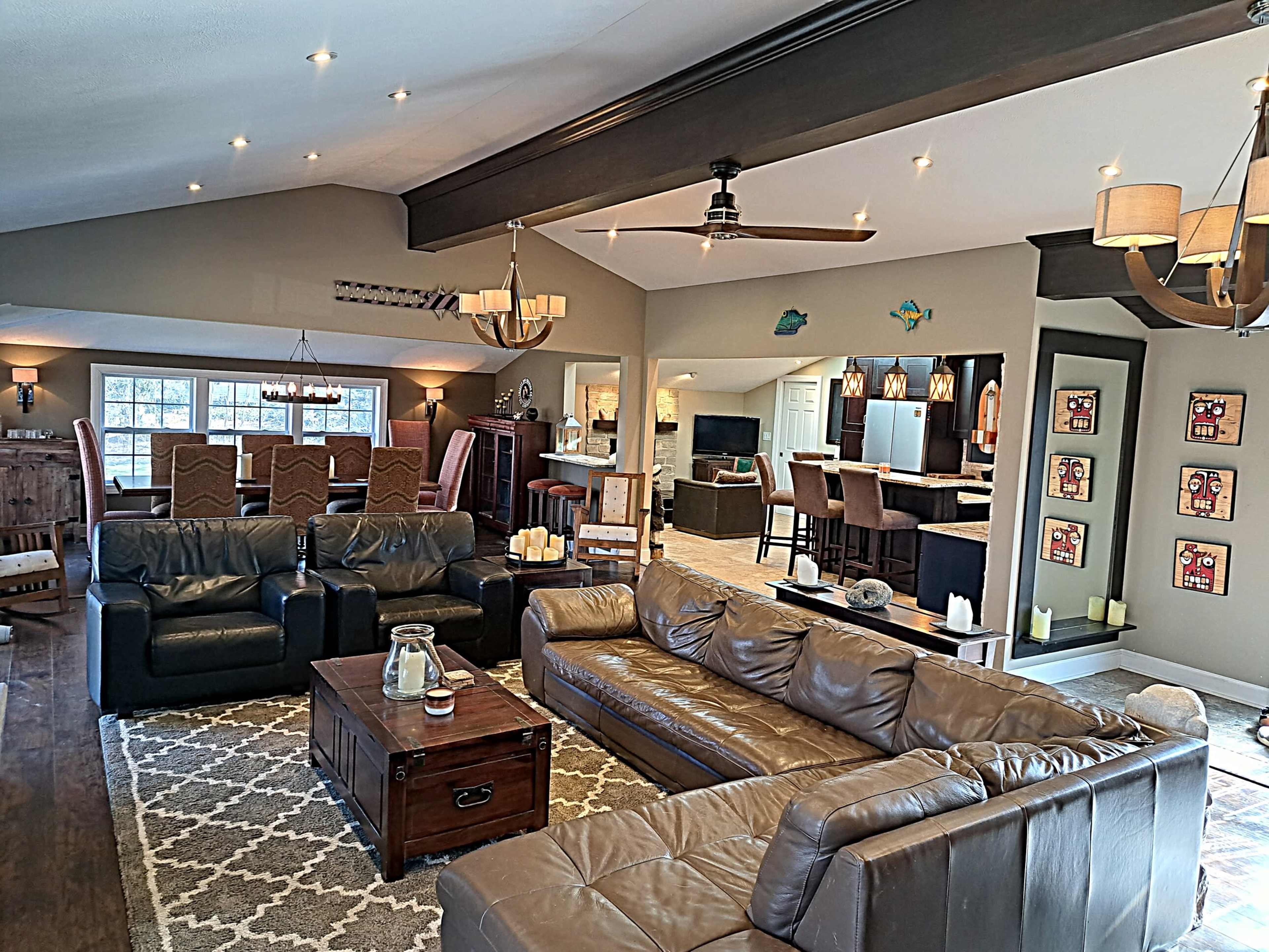 A spacious living room with multiple seating areas, a coffee table in front of a leather sofa, and a dining area visible in the background.