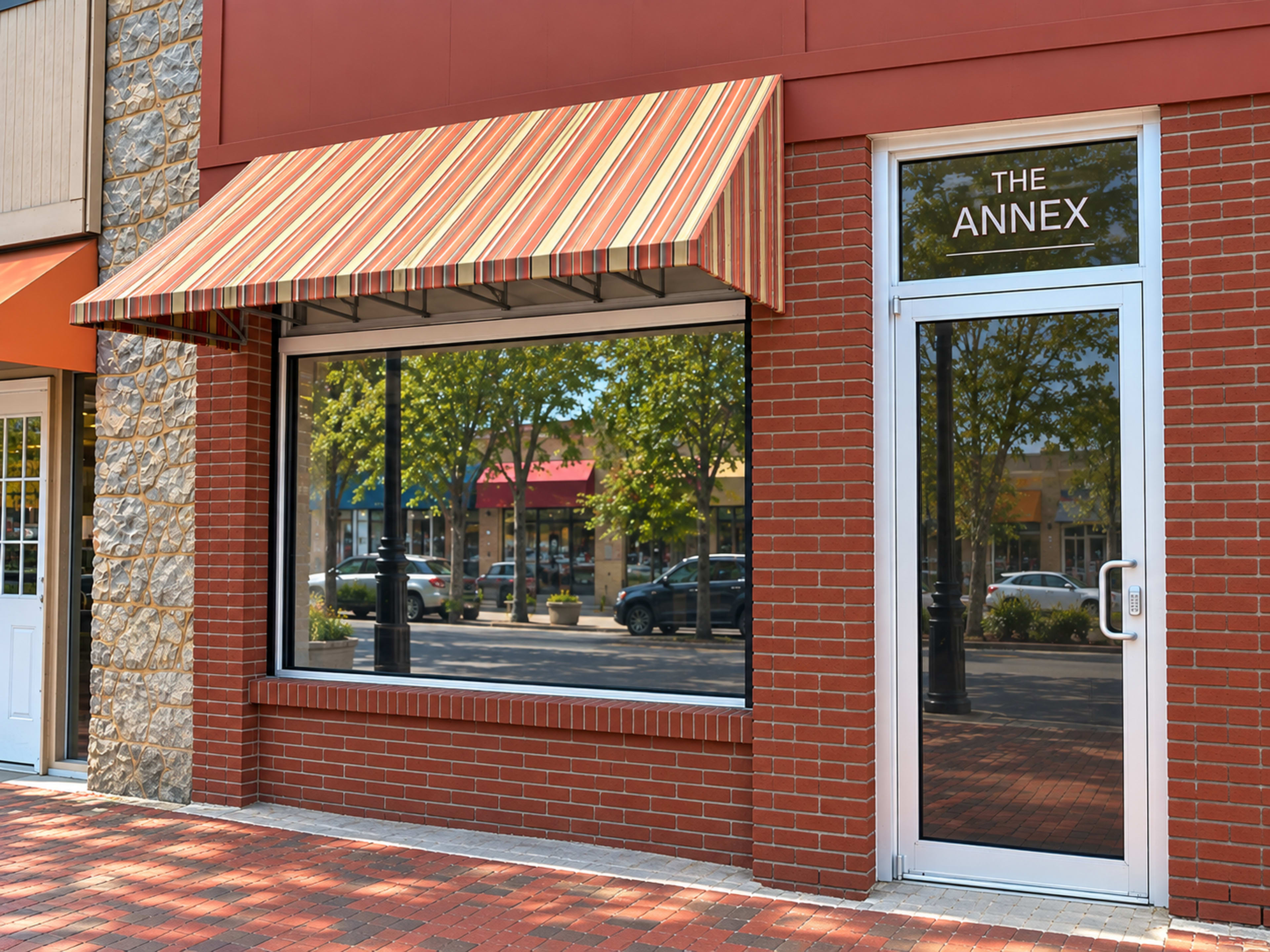 The image shows a storefront with a striped awning and a glass door, reflecting trees and buildings from across the street.