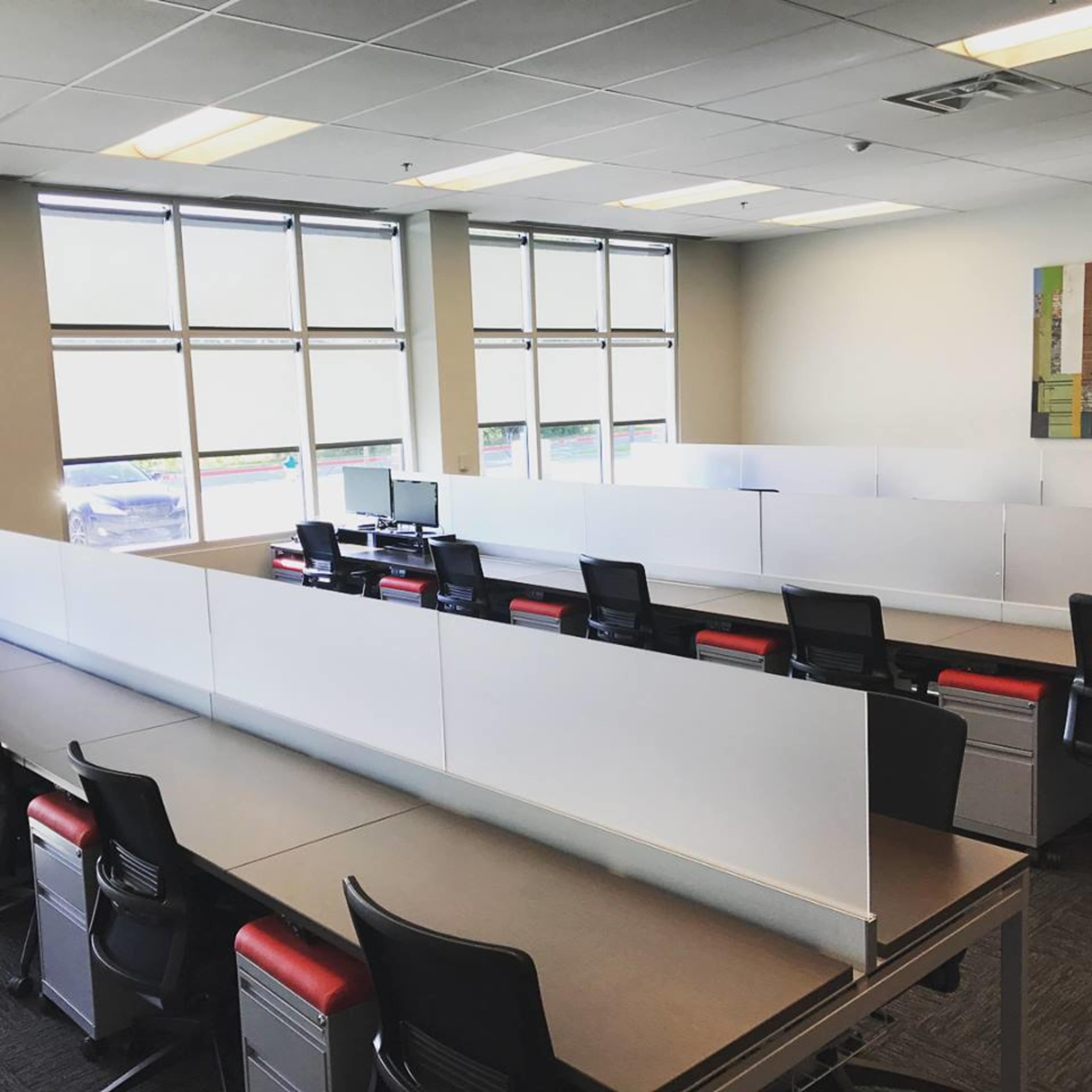 The image shows a modern office space with several white desks separated by partitions and black ergonomic chairs.